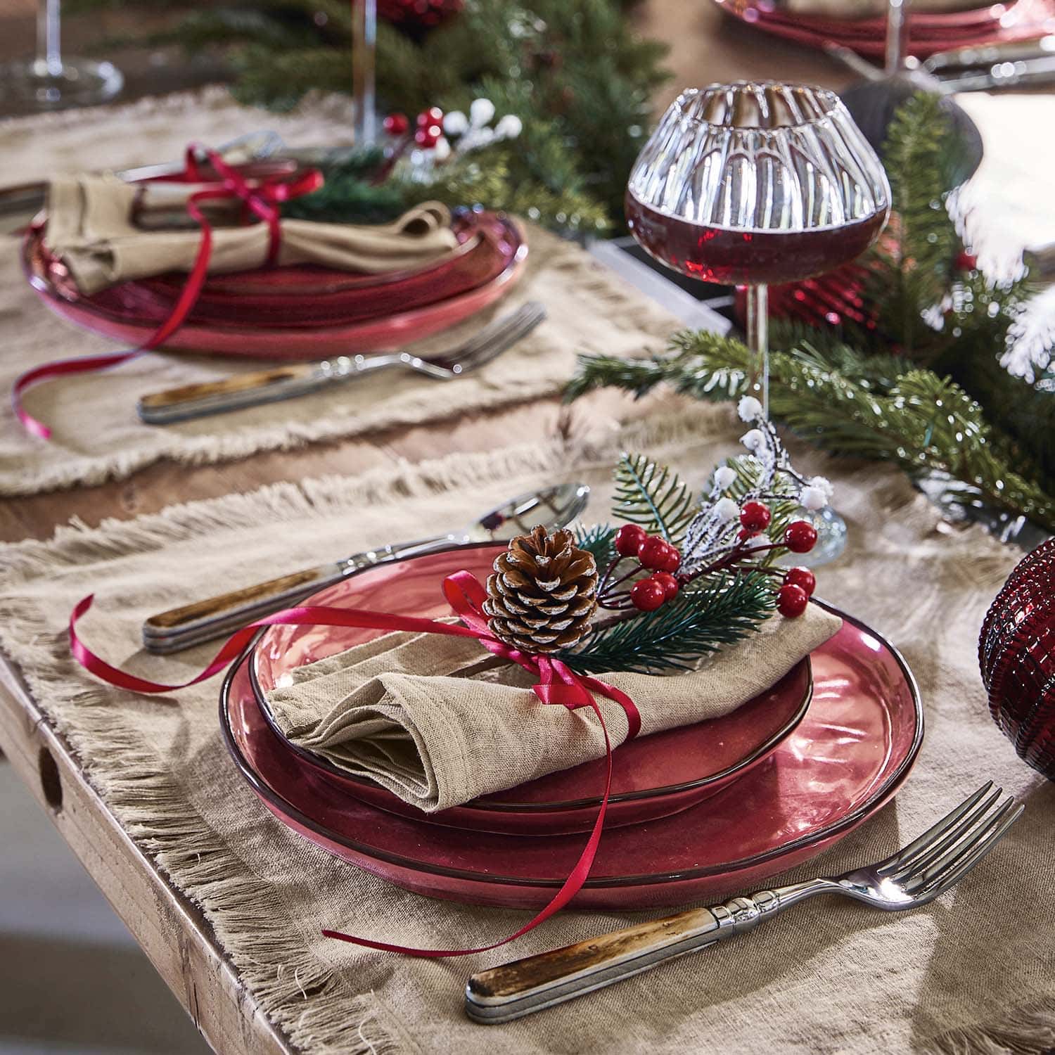 Table de fête avec assiettes en verre rouge et décoration de pomme de pin et baies rouges