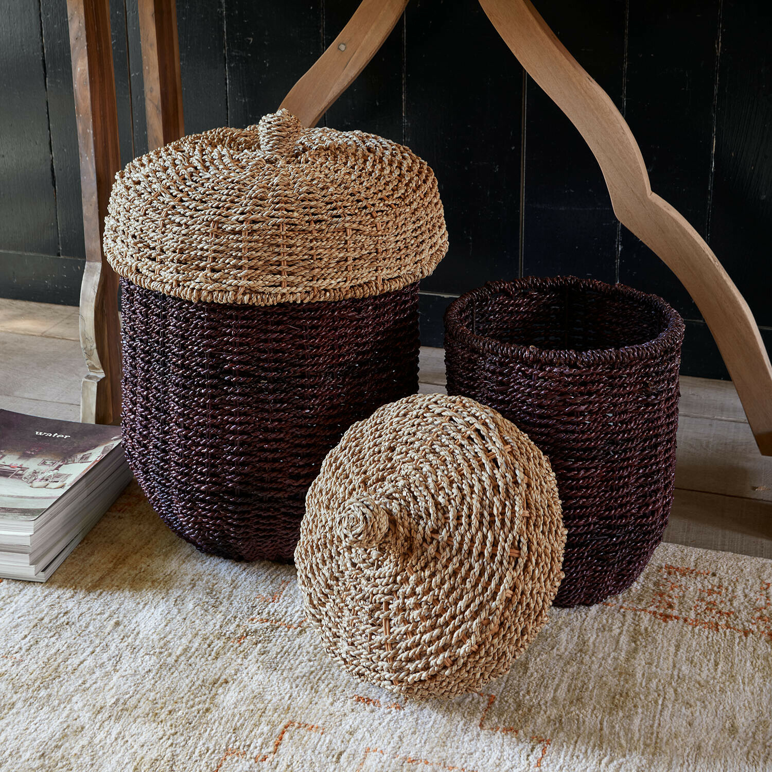 Lot de 2 paniers Aelwyn Ensemble de deux paniers marron avec couvercles en matériau tressé naturel posés sur un tapis