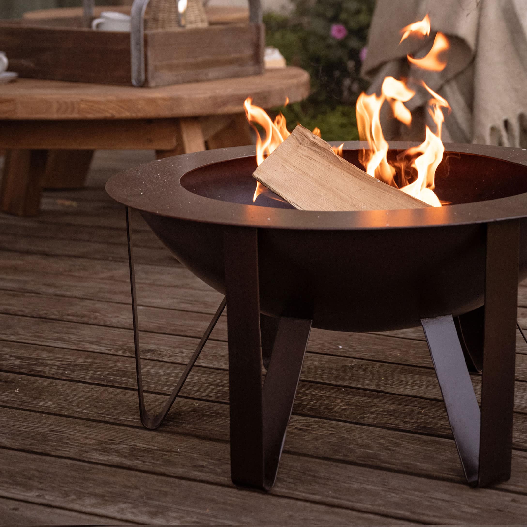 Brasero de jardin en métal noir avec bois en feu sur terrasse en bois