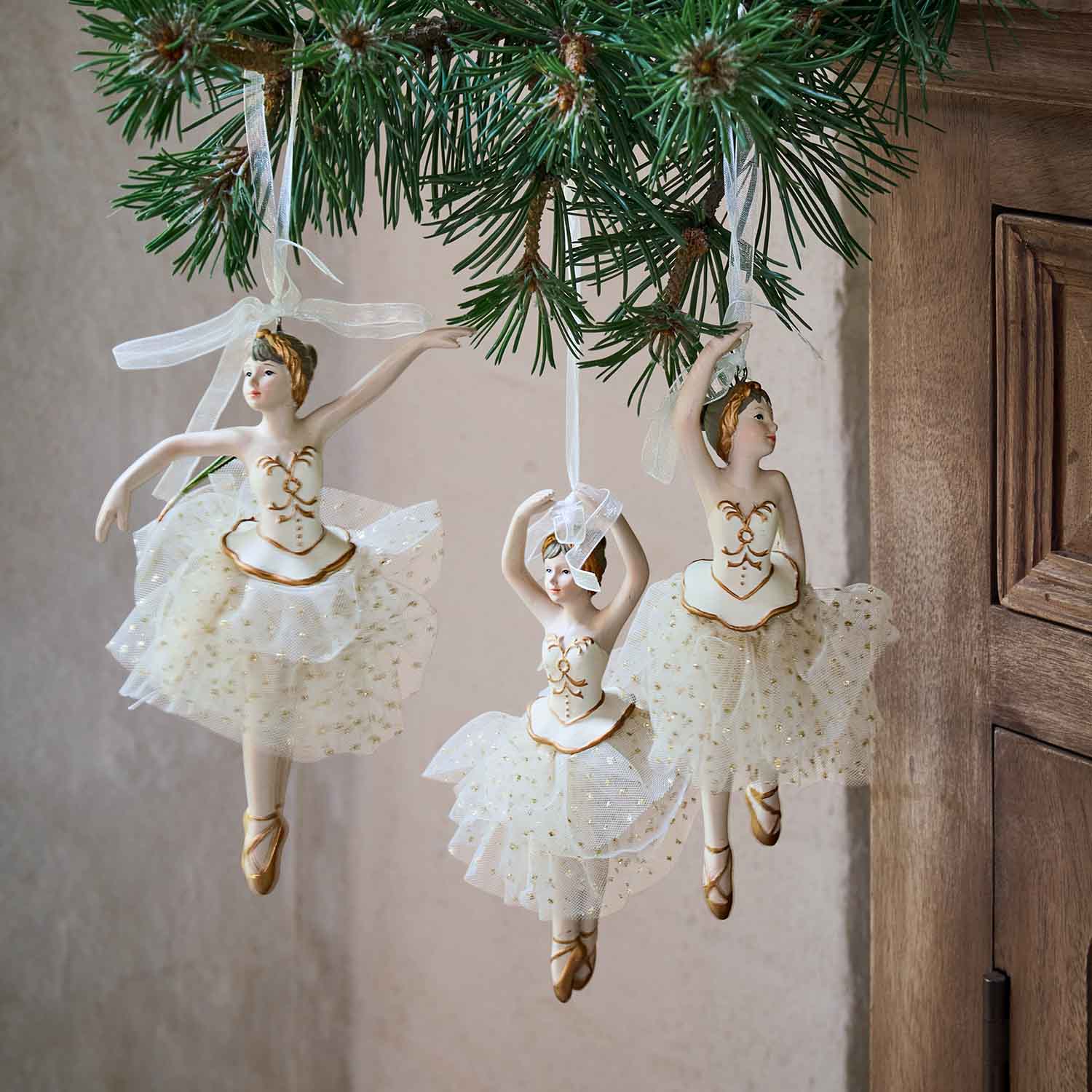 Trois décorations de ballerines blanches avec tutus en tulle et détails dorés suspendues à une branche de sapin
