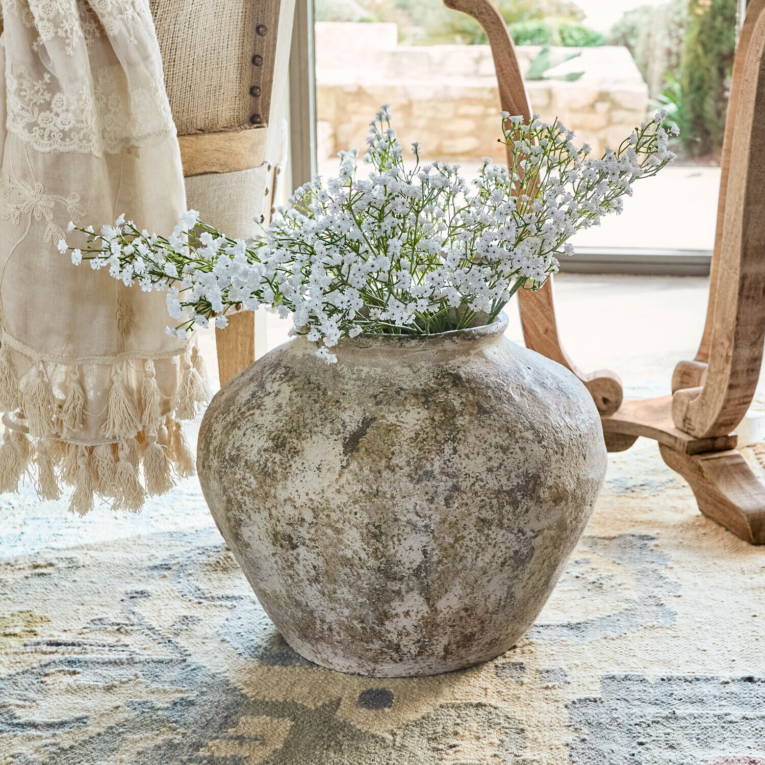 Grand vase en céramique rustique avec fleurs blanches posé sur un tapis dans un intérieur lumineux