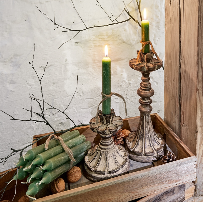 Deux bougeoirs décoratifs avec bougies vertes sur un plateau en bois avec noix et branches