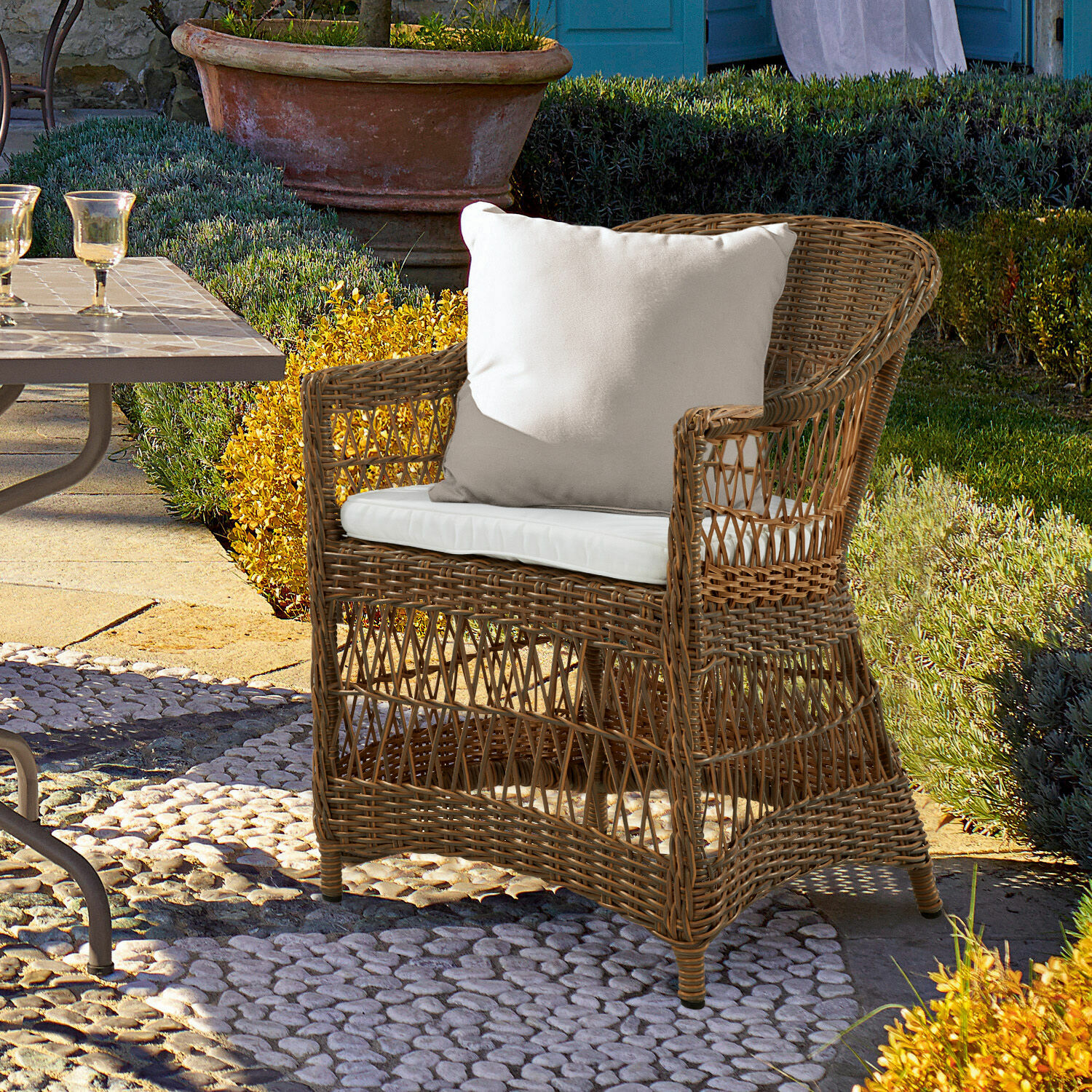 Fauteuil Garden Grove Fauteuil en rotin avec coussin blanc sur terrasse en pierre dans un jardin ensoleillé