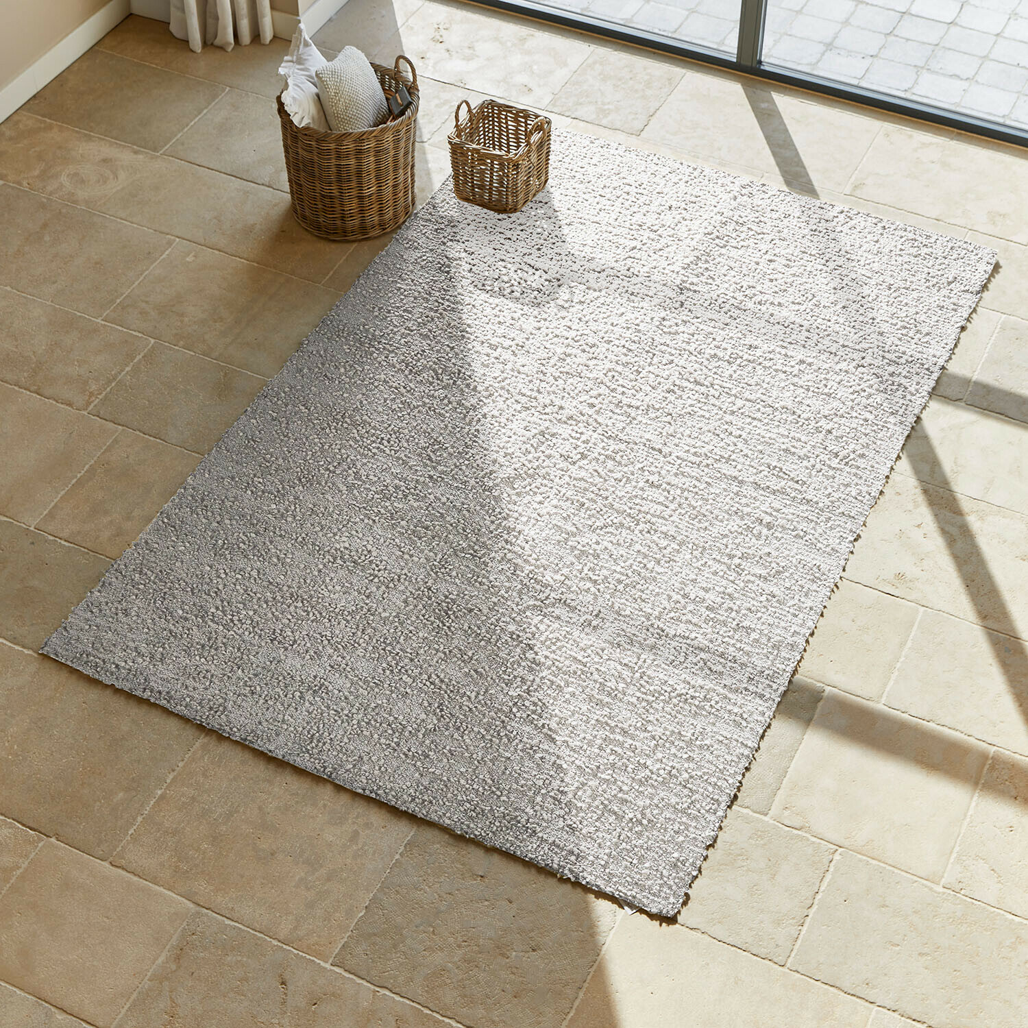 Tapis gris clair en matériau doux sur sol beige, apportant une ambiance chaleureuse à la pièce