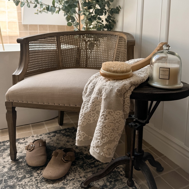 Chaise en bois avec assise claire, serviette à motif, brosse corporelle et bougie parfumée sur table