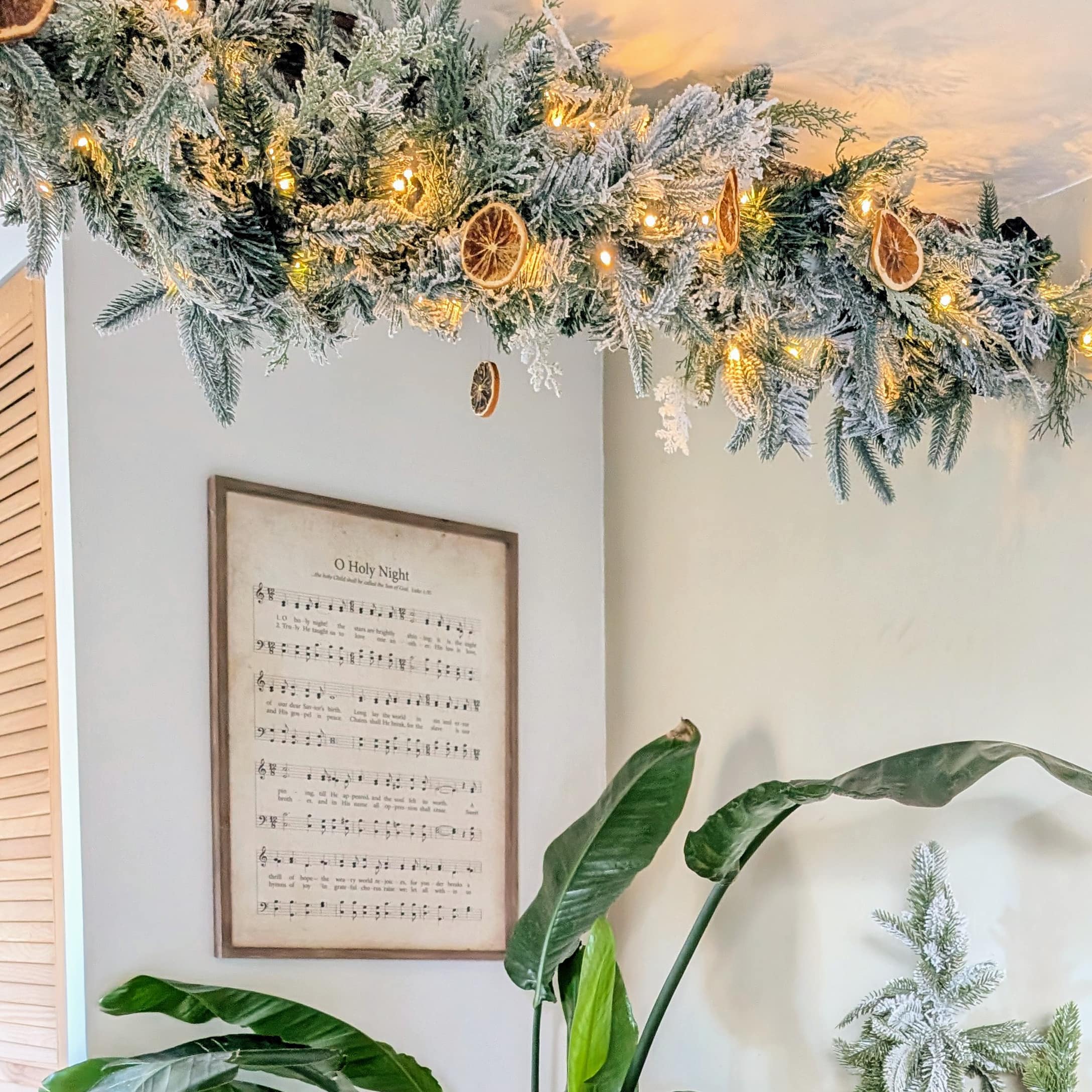 Décoration de Noël suspendue avec branches enneigées, guirlande lumineuse et tranches d'orange séchées