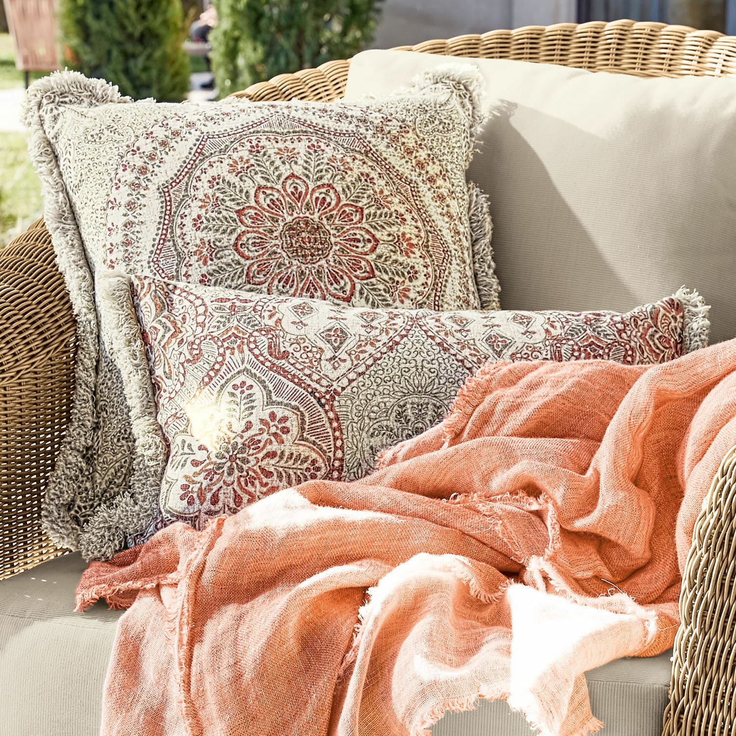 Lot de 2 housses de coussins Margret Coussins décoratifs en coton beige et rouge avec motif double face et plaid orange sur canapé en osier