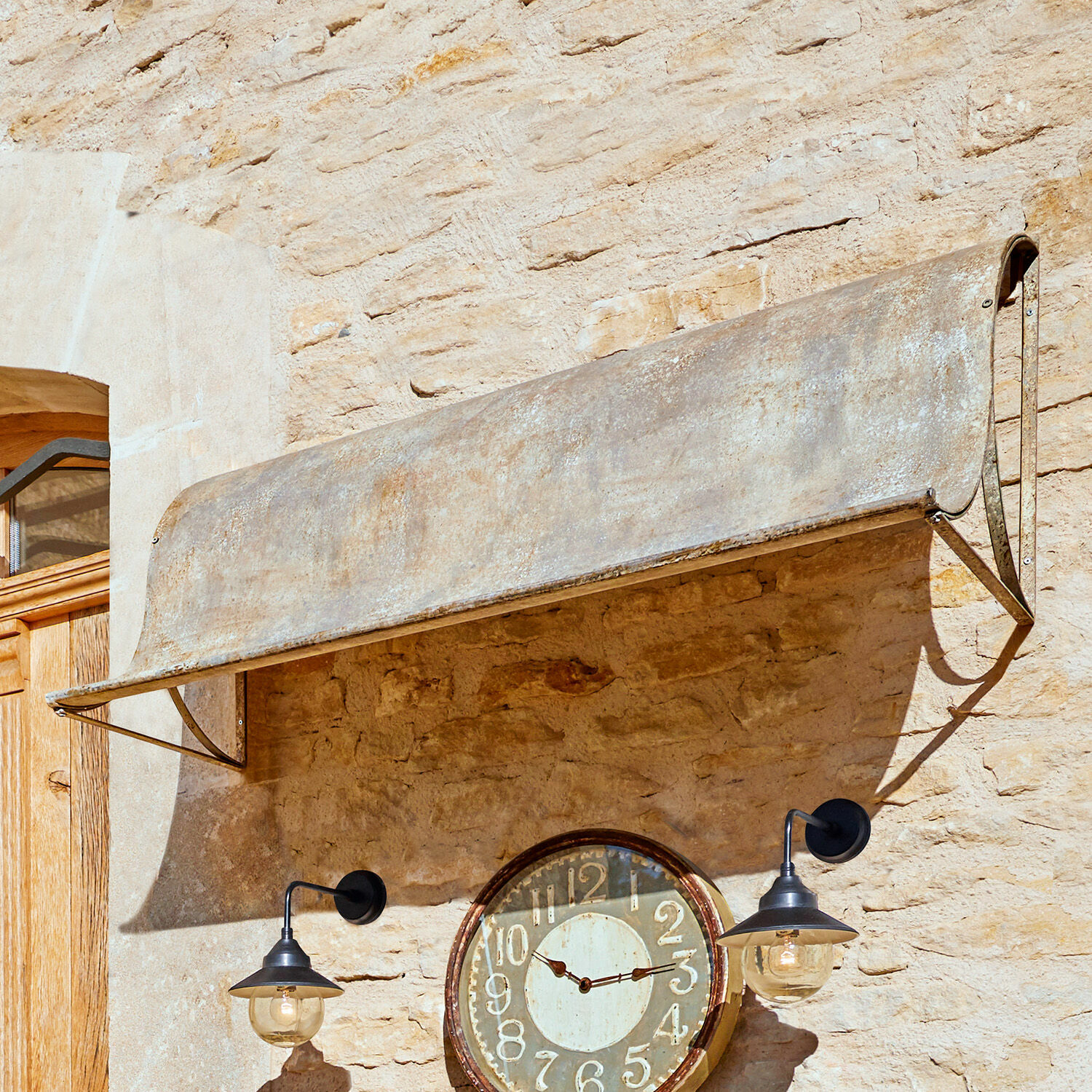 Auvent Lison Auvent en métal vieilli gris fixé sur un mur en pierre avec horloge et lampes noires
