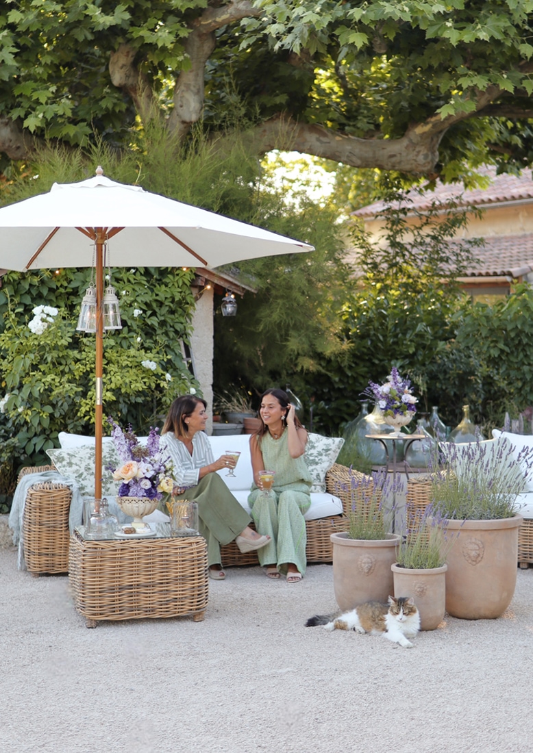 Ensemble de mobilier de jardin en rotin naturel avec coussins blancs et parasol, décor floral et chat sur la terrasse