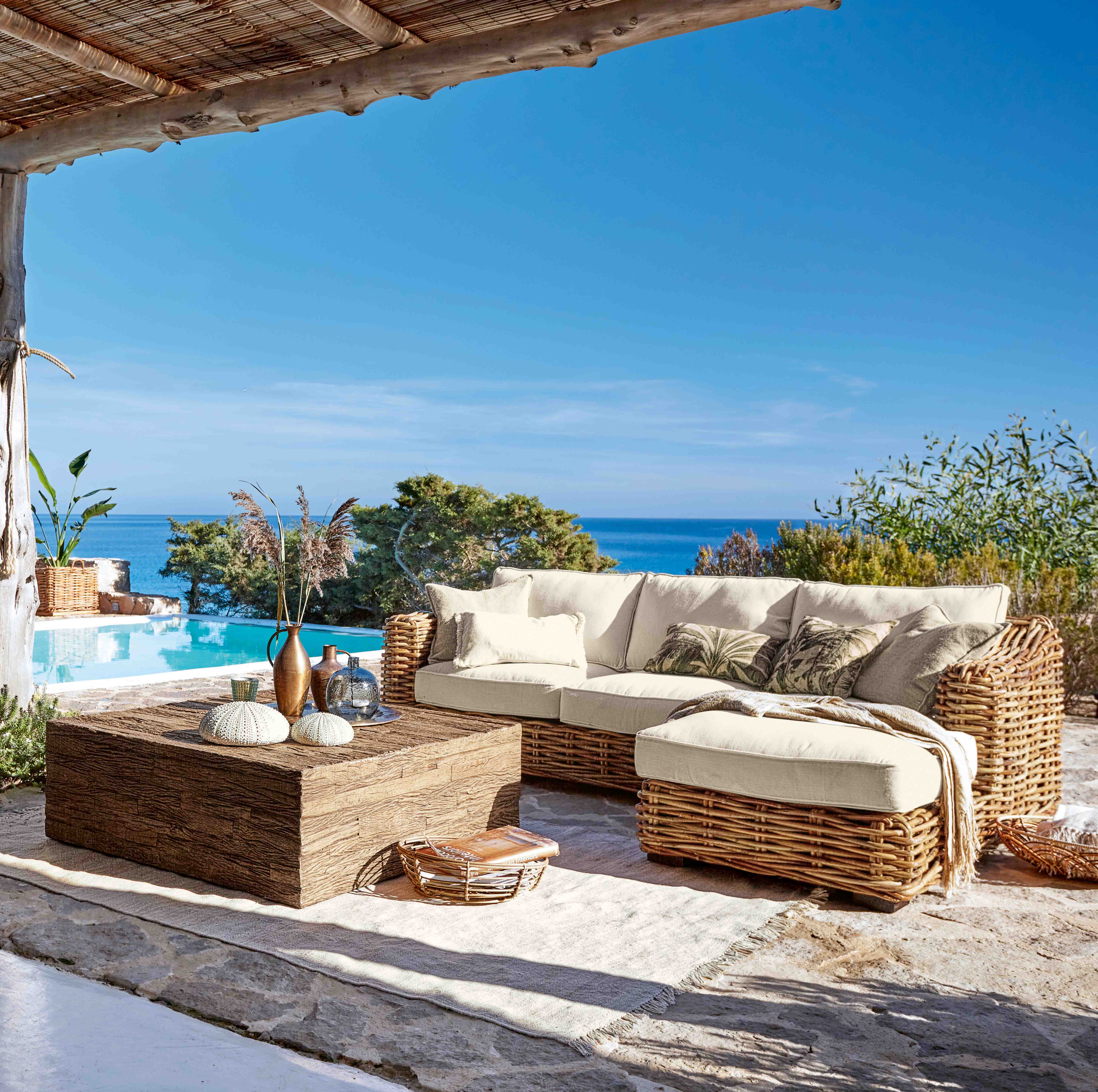 Ensemble de meubles d'extérieur en rotin avec coussins crème, vue sur piscine et mer bleue