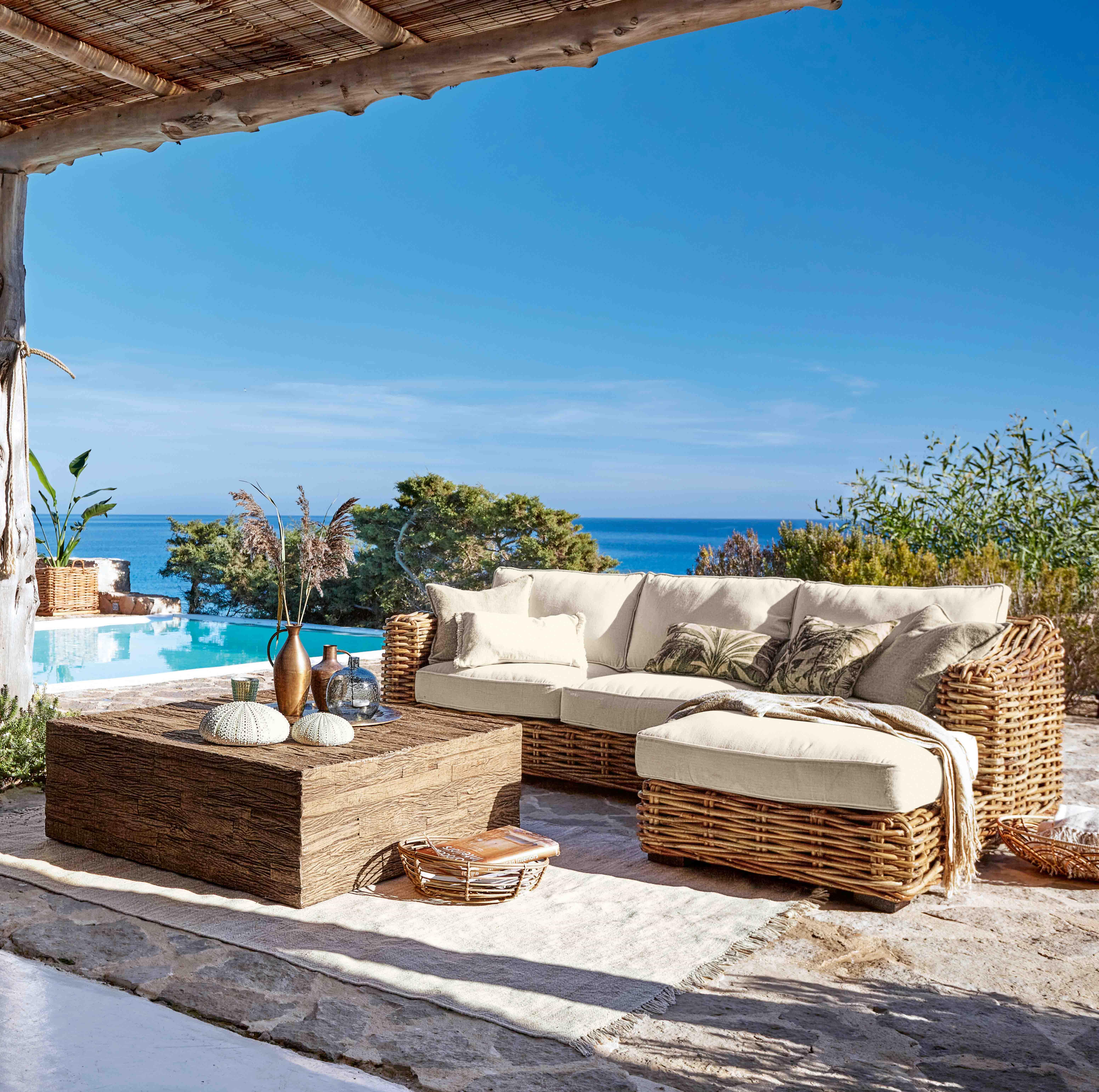 Ensemble de meubles d'extérieur en rotin avec coussins crème, vue sur piscine et mer bleue