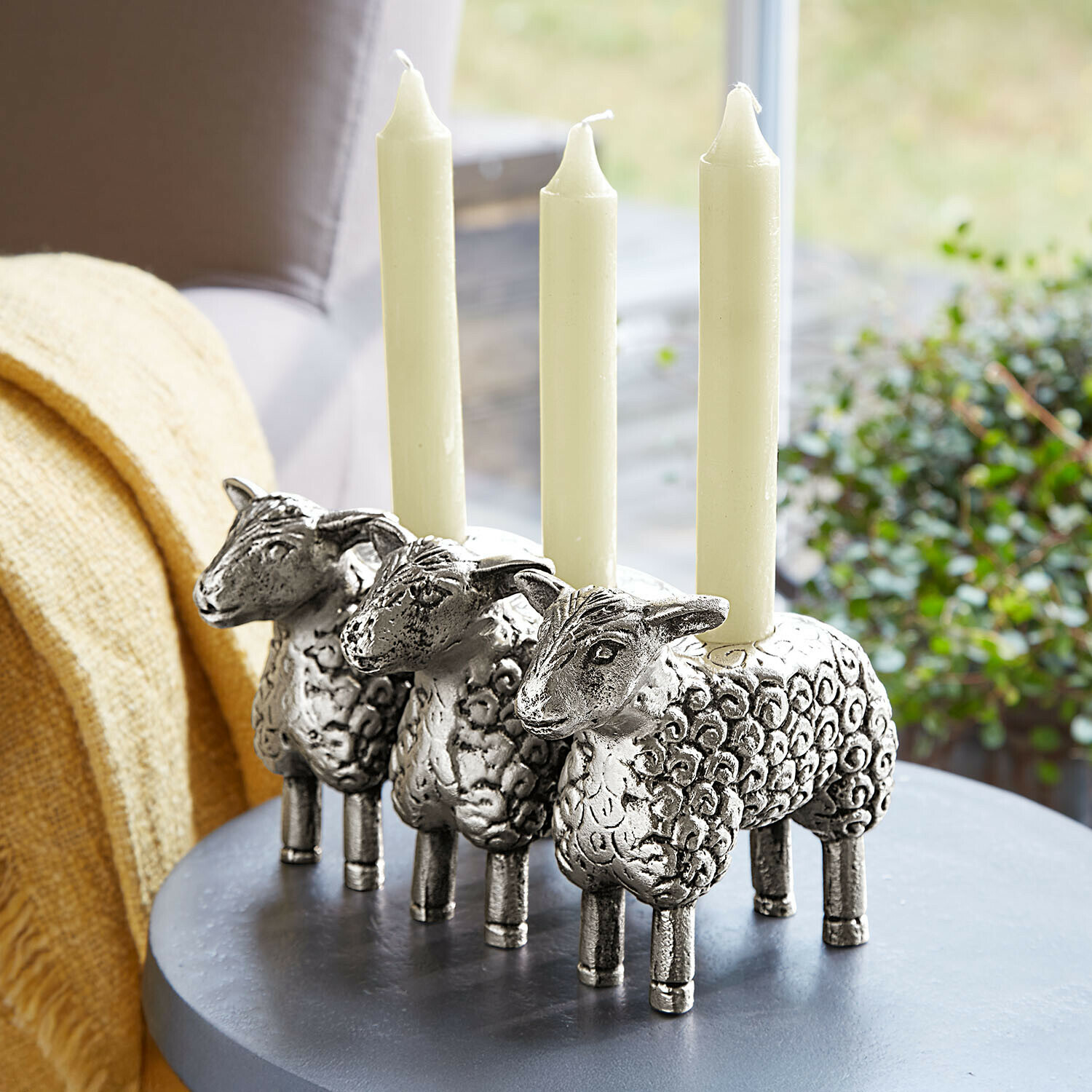 Bougeoir Séverac Trois bougeoirs argentés en forme de moutons avec des bougies blanches sur une table grise