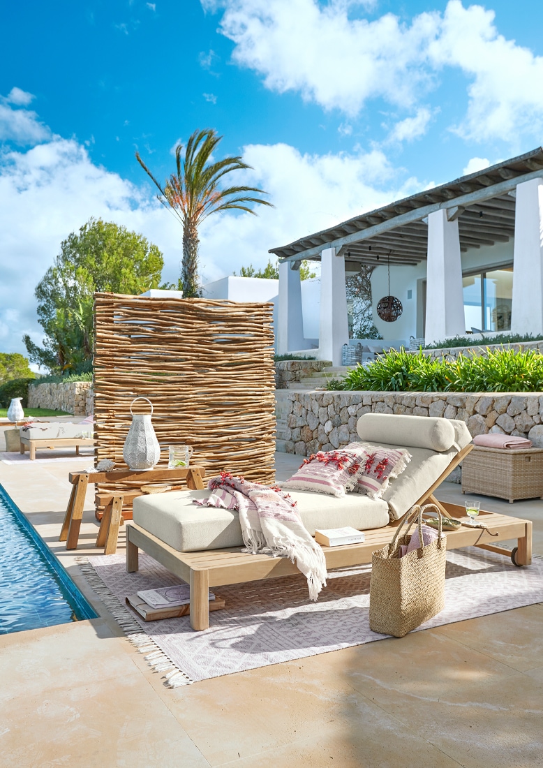 Chaise longue en bois clair avec coussin crème et plaid décoratif au bord de la piscine sur la terrasse