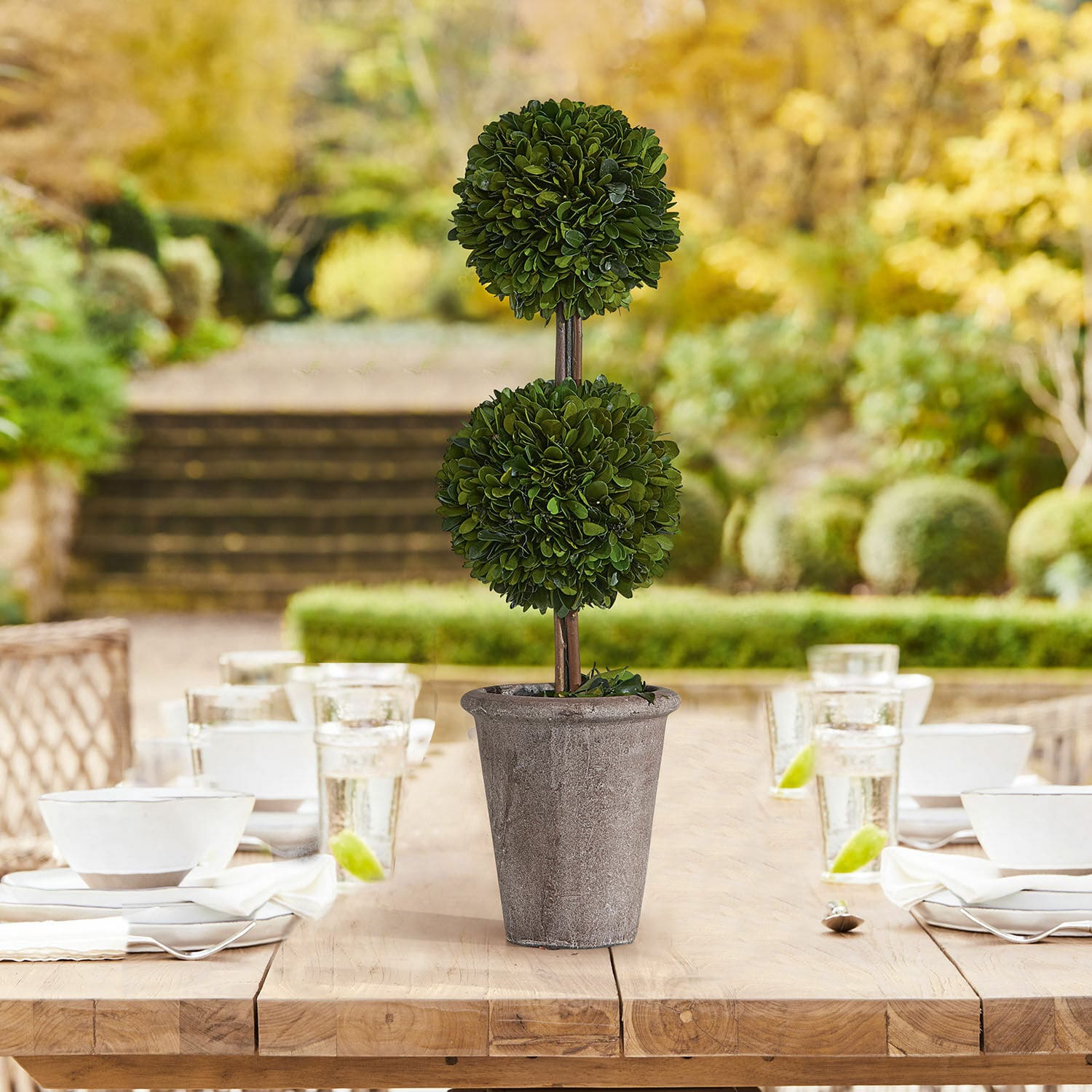 Arbre décoratif Noisse Plante décorative artificielle en pot en pierre grise sur une table en bois dans un jardin