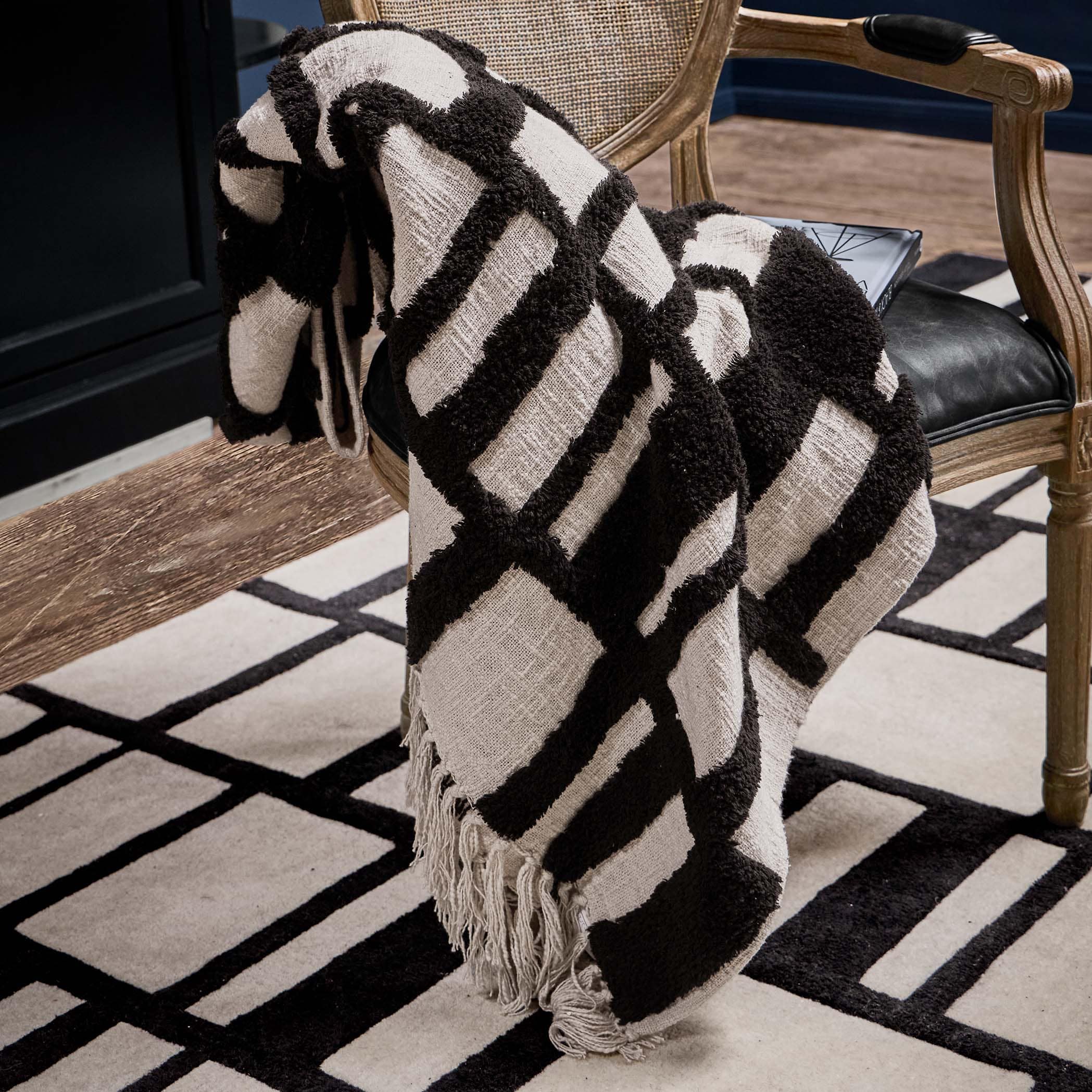 Plaid noir et blanc à motif géométrique en tissu doux posé sur une chaise en bois dans un salon