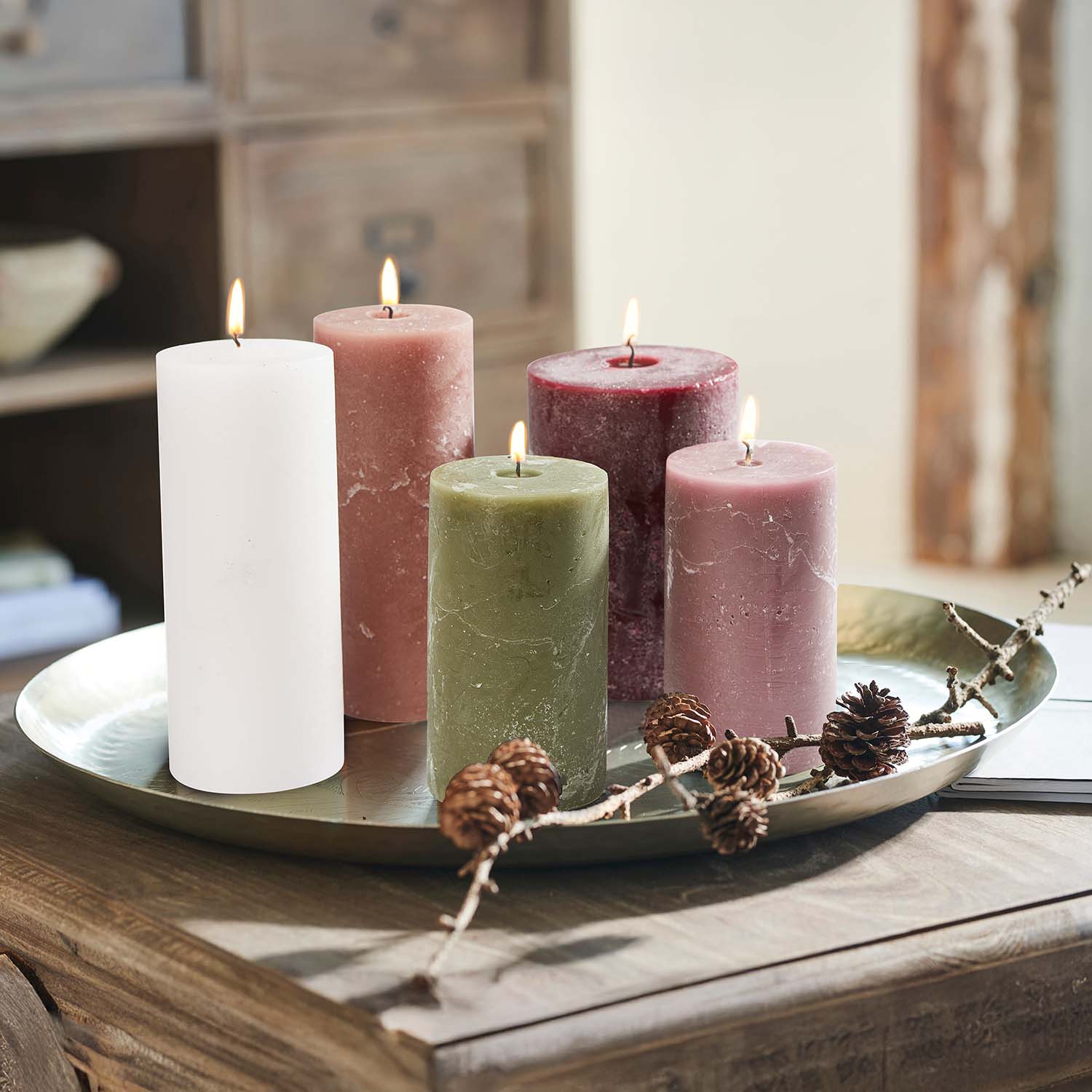 Ensemble de cinq bougies colorées sur un plateau en métal avec des pommes de pin décoratives sur une table en bois