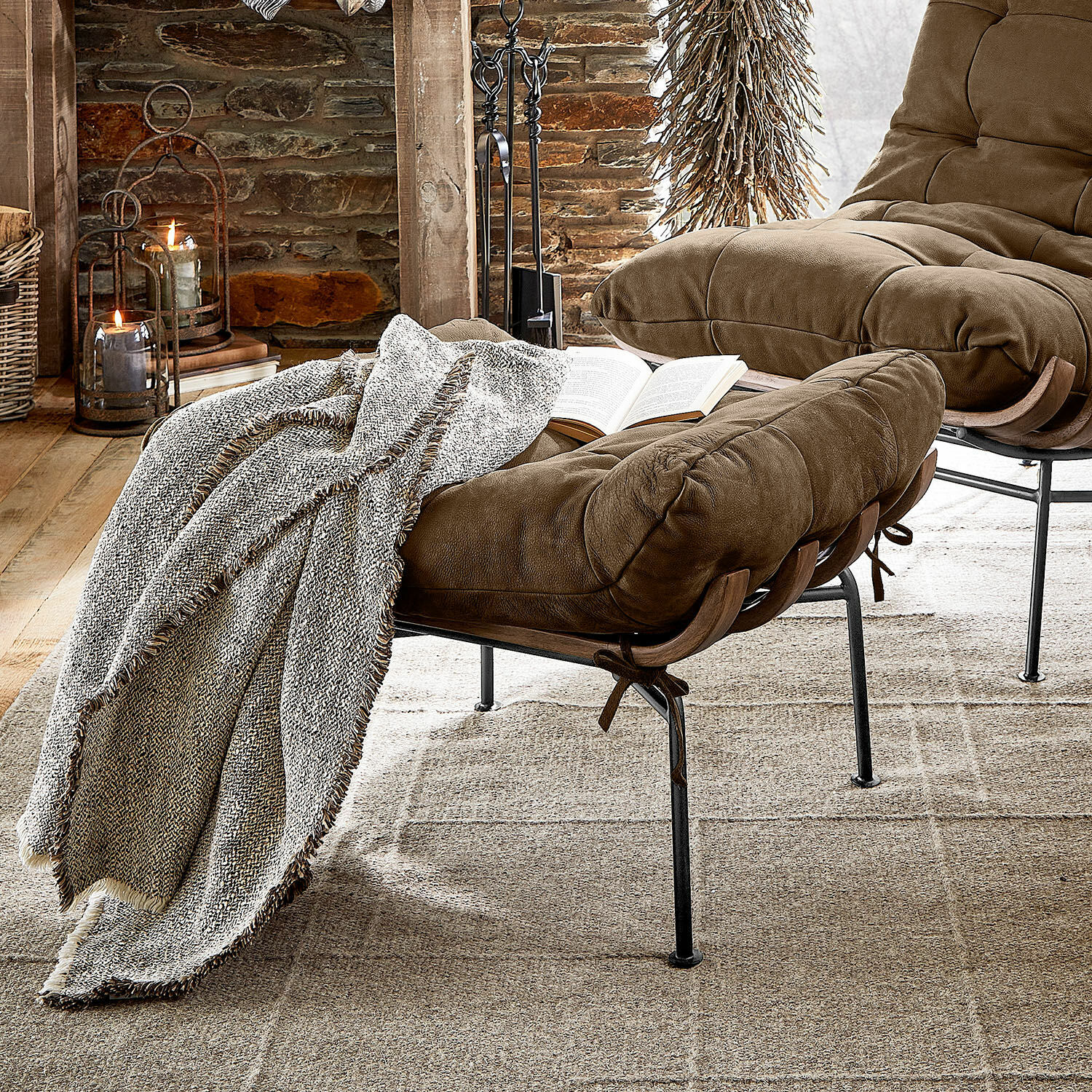 Tabouret Horraine Fauteuil marron en tissu doux avec repose-pieds et couverture grise sur tapis beige dans un intérieur rustique