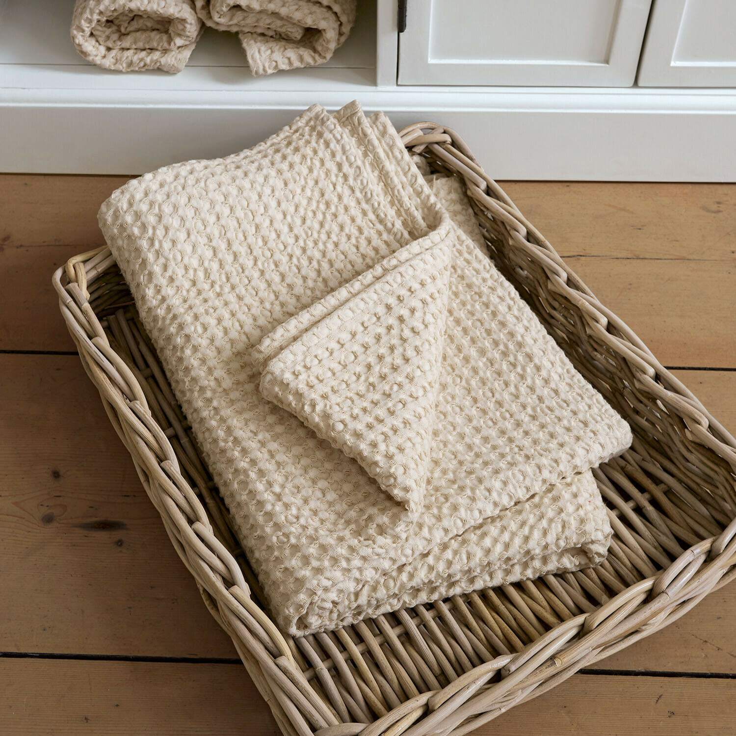 Plaid crème en coton gaufré dans un panier en osier posé sur un sol en bois clair