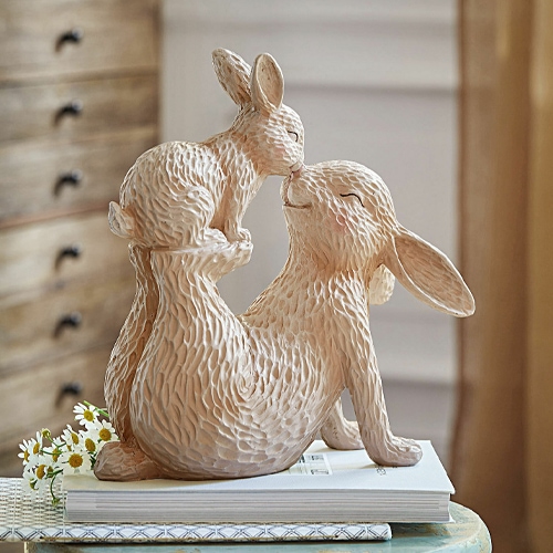 Figurine en céramique beige de deux lapins câlins posée sur des livres, décoration printanière douce