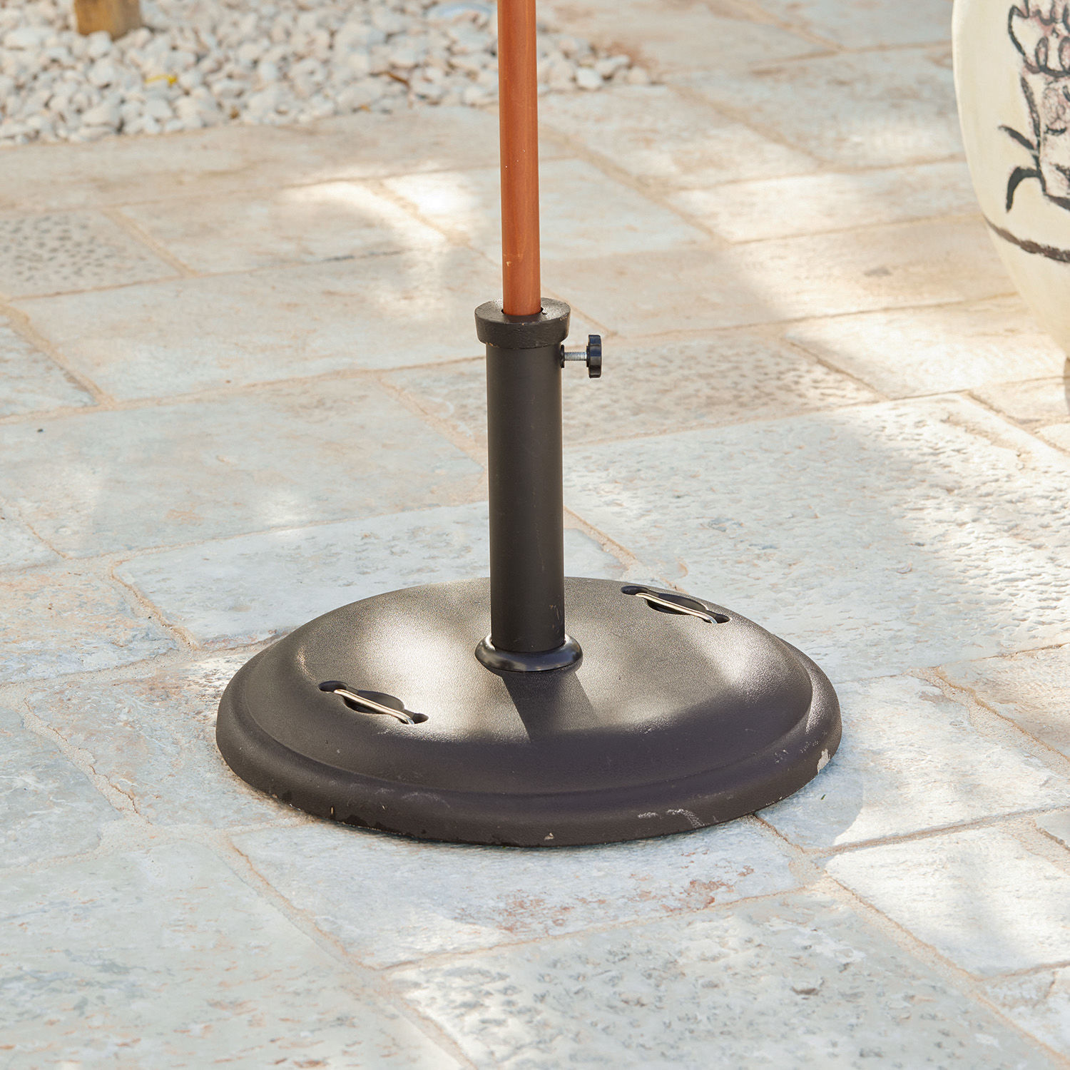 Pied pour parasol Yarra Base de parasol en métal noir posée sur un sol en pierre pour jardin ou terrasse