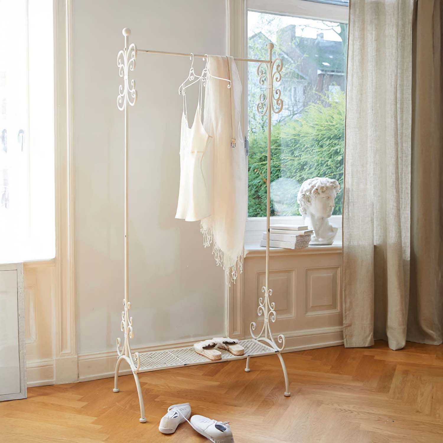 Porte-vêtements en métal blanc avec détails décoratifs dans une pièce lumineuse au sol en bois