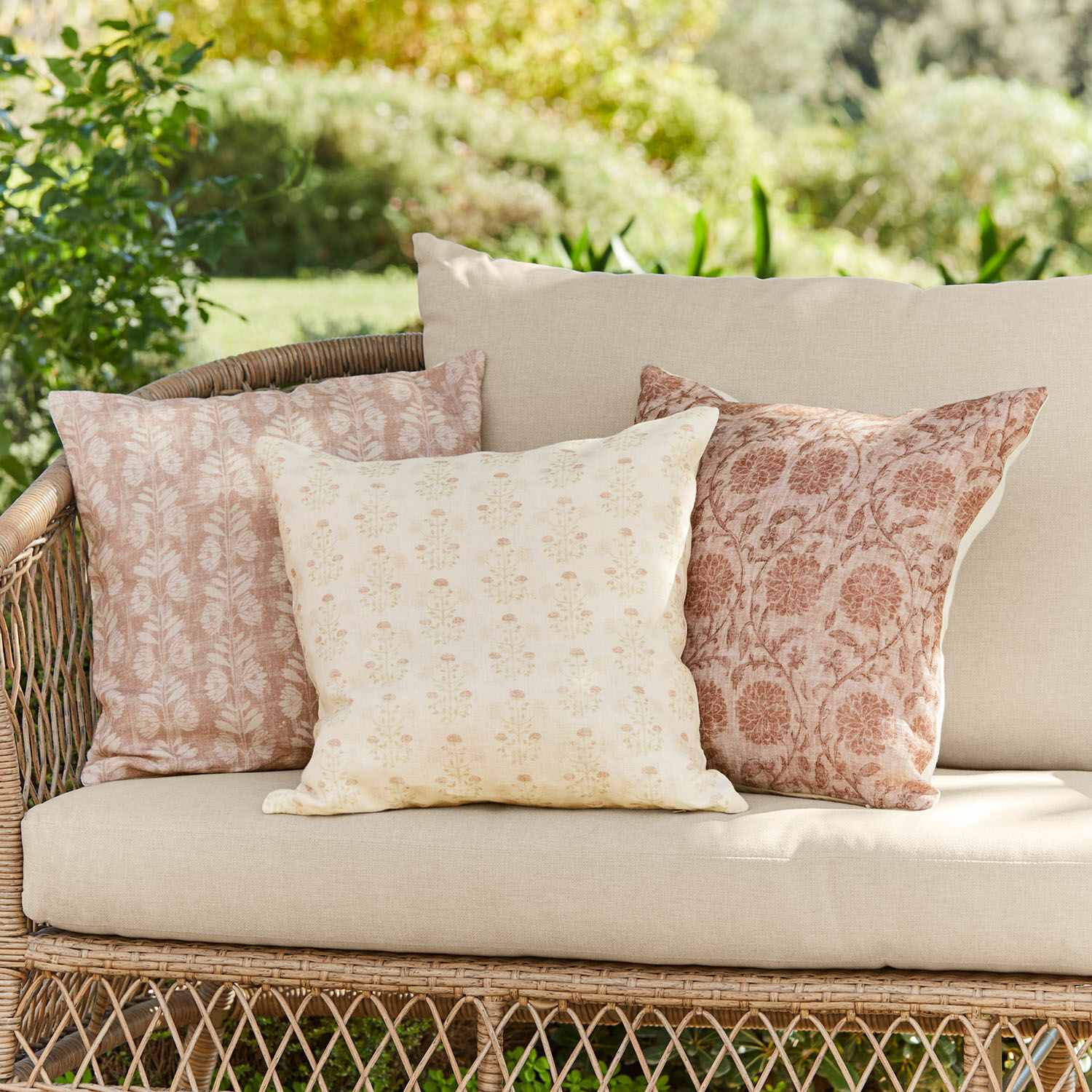 Lot de 3 housses de coussins Tarouja Ensemble de trois coussins décoratifs en coton beige et rose sur un canapé en osier dans un jardin