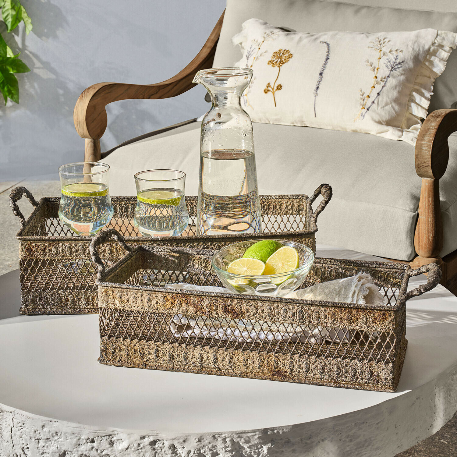 Deux plateaux métalliques rustiques avec poignées sur table blanche avec carafe et verres d'eau citronnée