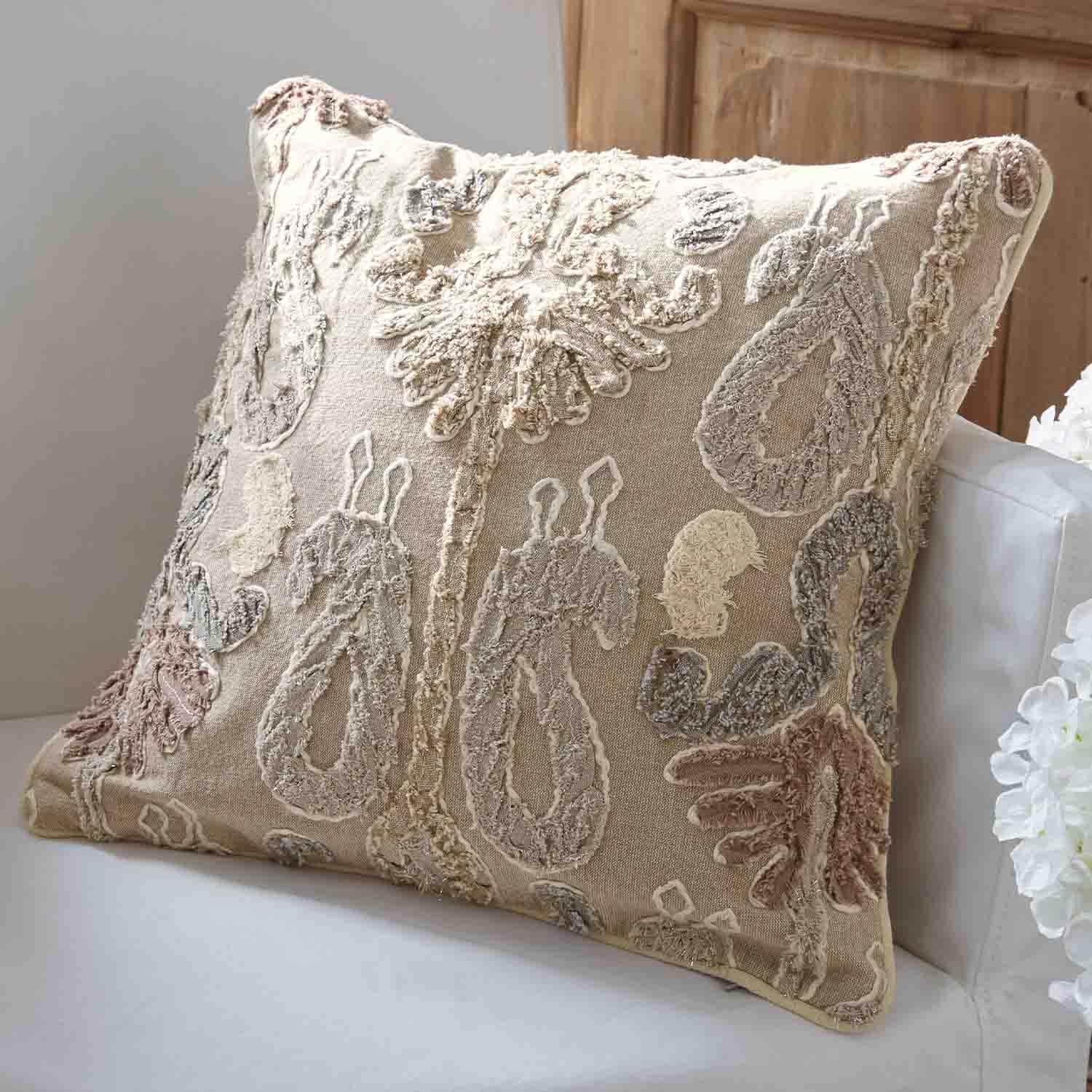Coussin décoratif beige avec motif brodé en couleurs pastel sur un canapé blanc