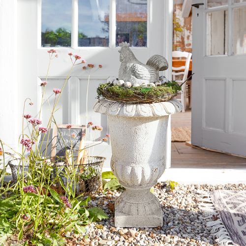 Vase décoratif blanc en pierre avec figurine de poule et nid d'œufs à l'extérieur près de la porte