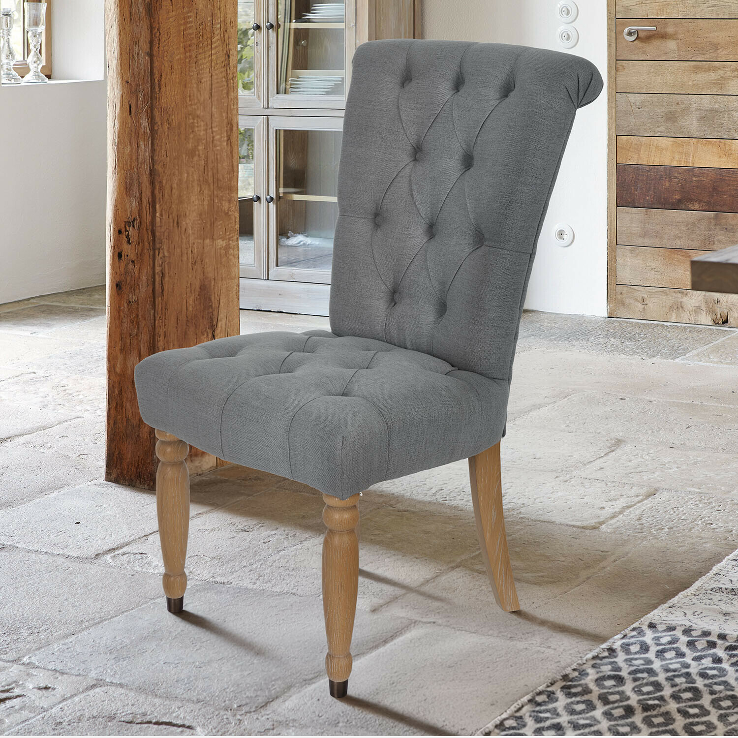 Chaise rembourrée grise avec pieds en bois dans un intérieur rustique avec sol en pierre