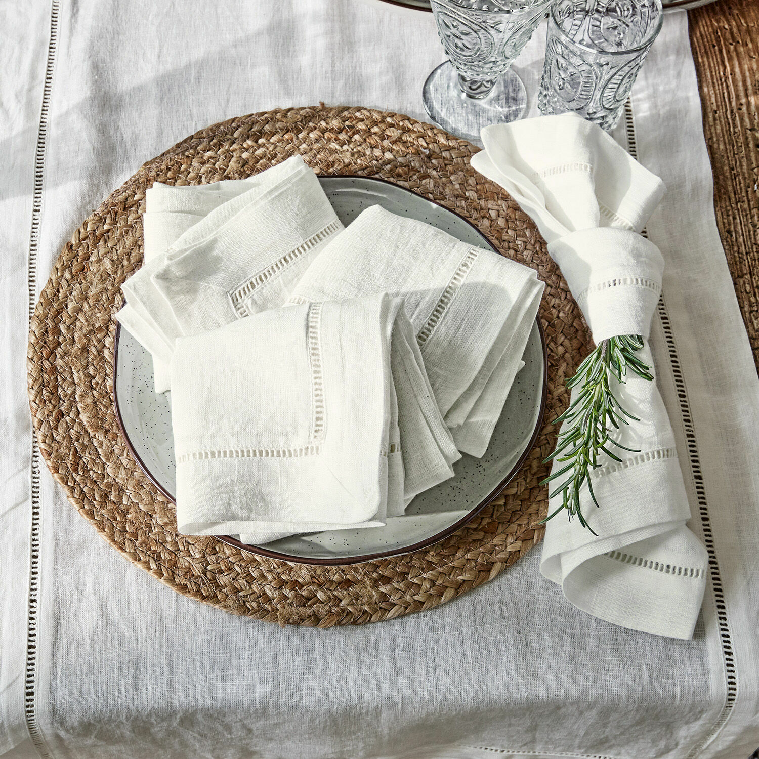 Lot de 4 serviettes Covent Garden Serviettes en lin crème sur assiette avec dessous de plat tressé et décoration romarin