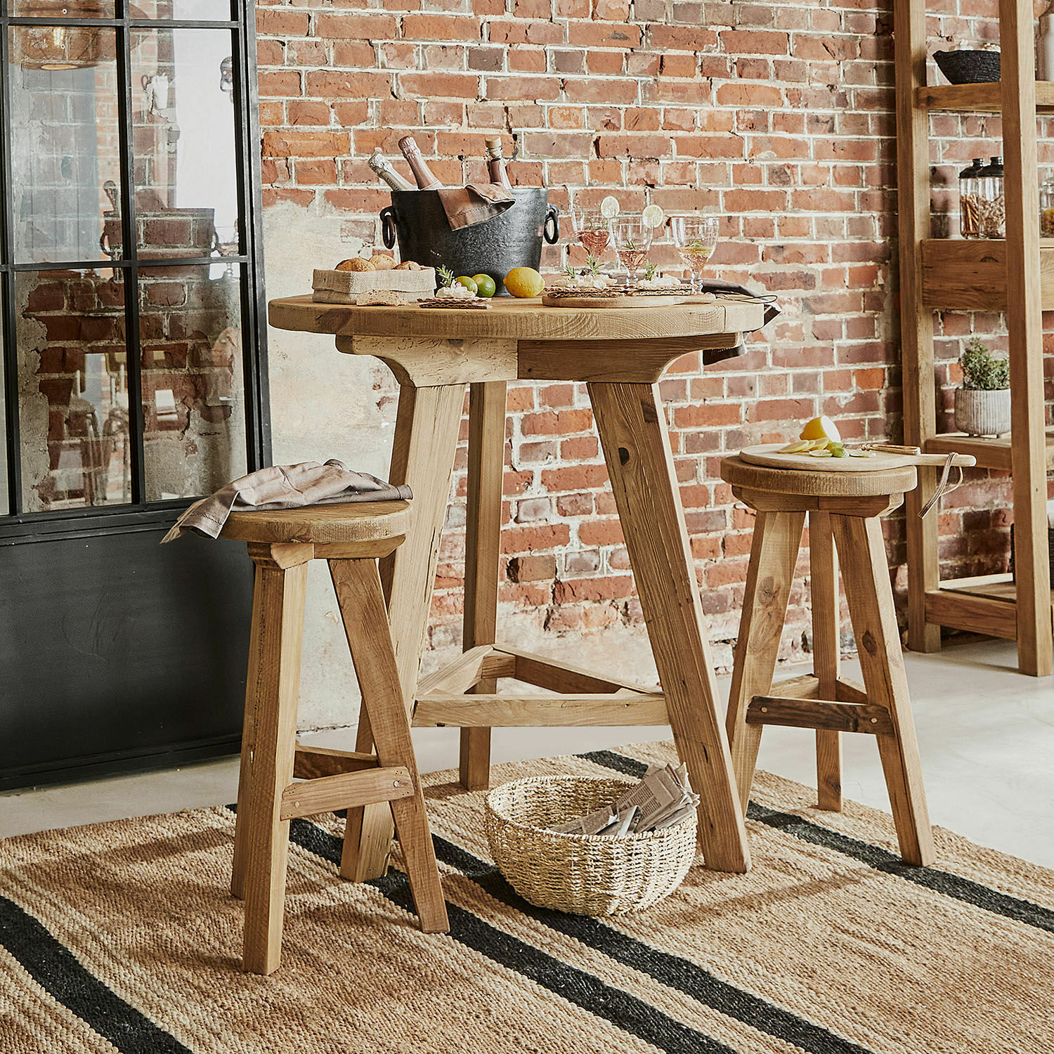 Ensemble table et chaises Stonington Table haute en bois naturel avec deux tabourets assortis sur tapis en jute dans un intérieur industriel