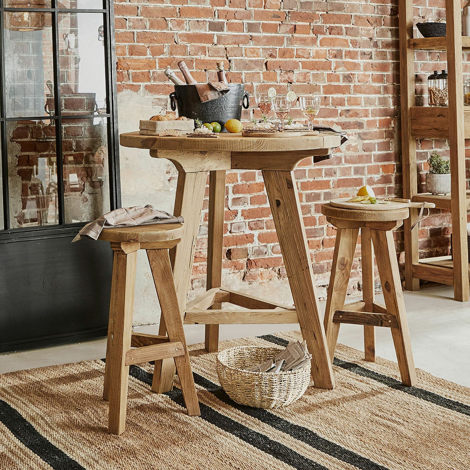 Ensemble table et chaises Stonington Table haute en bois naturel avec deux tabourets assortis sur tapis en jute dans un intérieur industriel