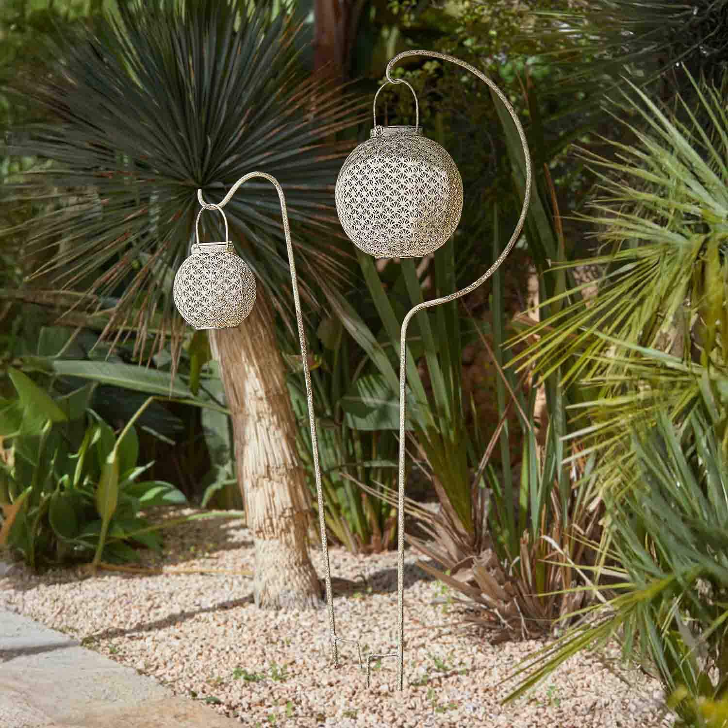 Lanterne de jardin en métal blanc avec motif ajouré suspendue sur des supports dans un cadre végétal