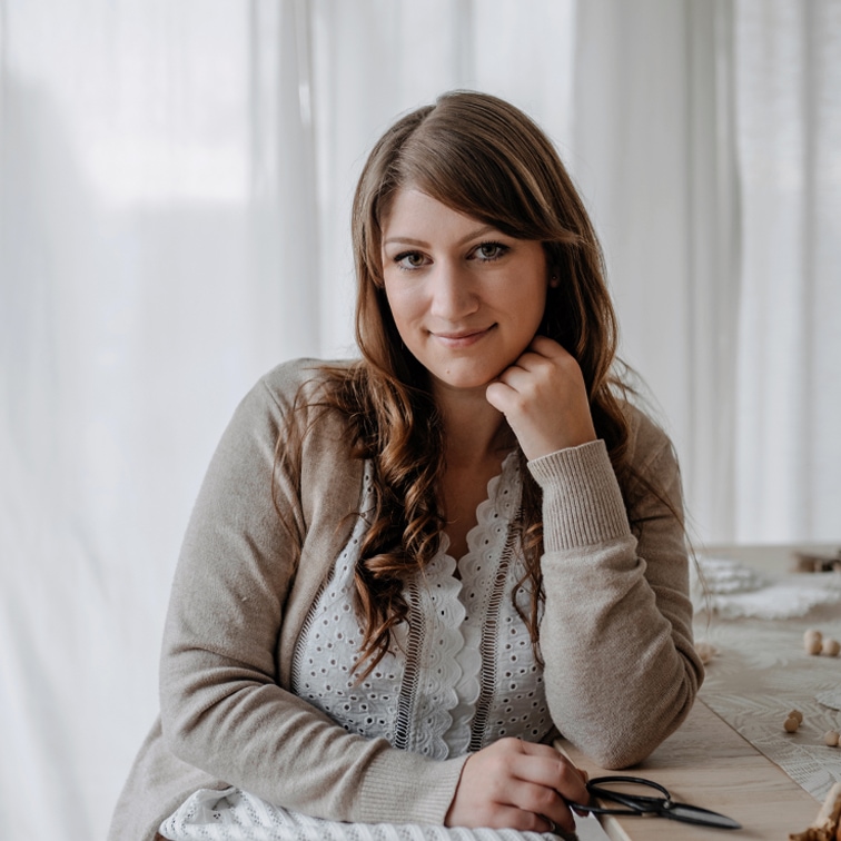 Portrait d'une femme en cardigan beige et blouse blanche en dentelle assise à une table dans un intérieur lumineux