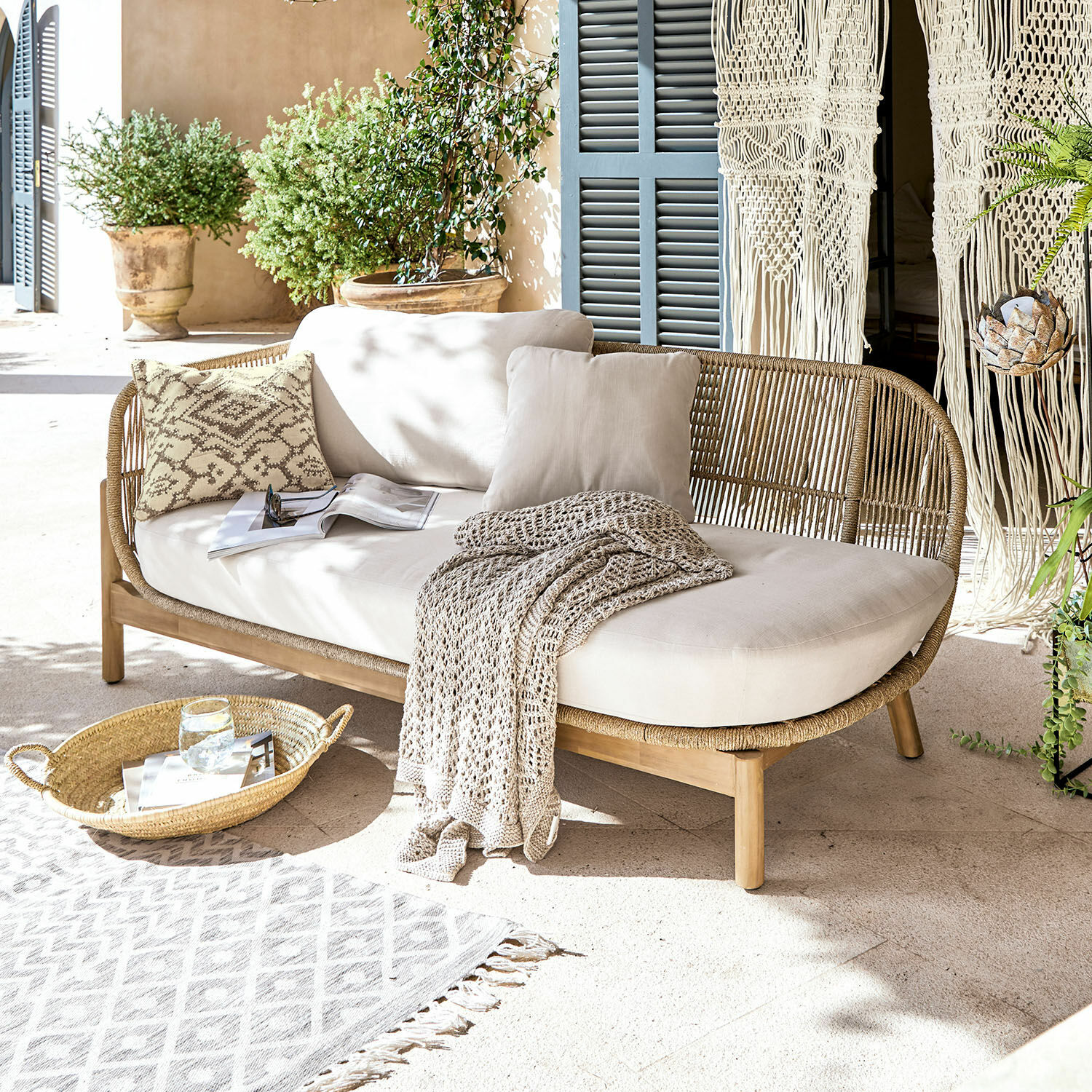 Méridienne FSC®-100% Belvidere Canapé en rotin et bois avec coussins crème et plaid sur terrasse lumineuse avec plantes