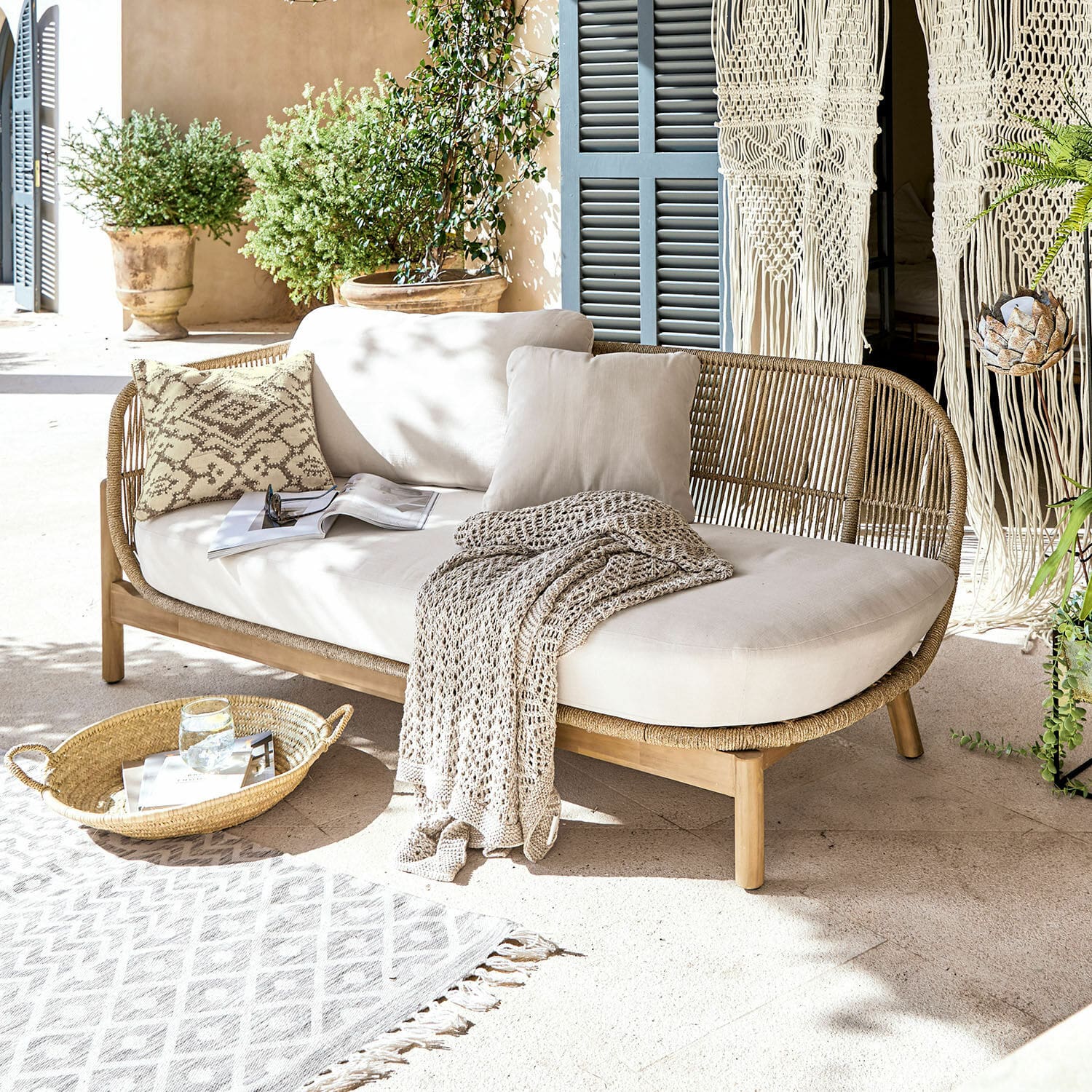Méridienne FSC®-100% Belvidere Canapé en rotin et bois avec coussins crème et plaid sur terrasse lumineuse avec plantes
