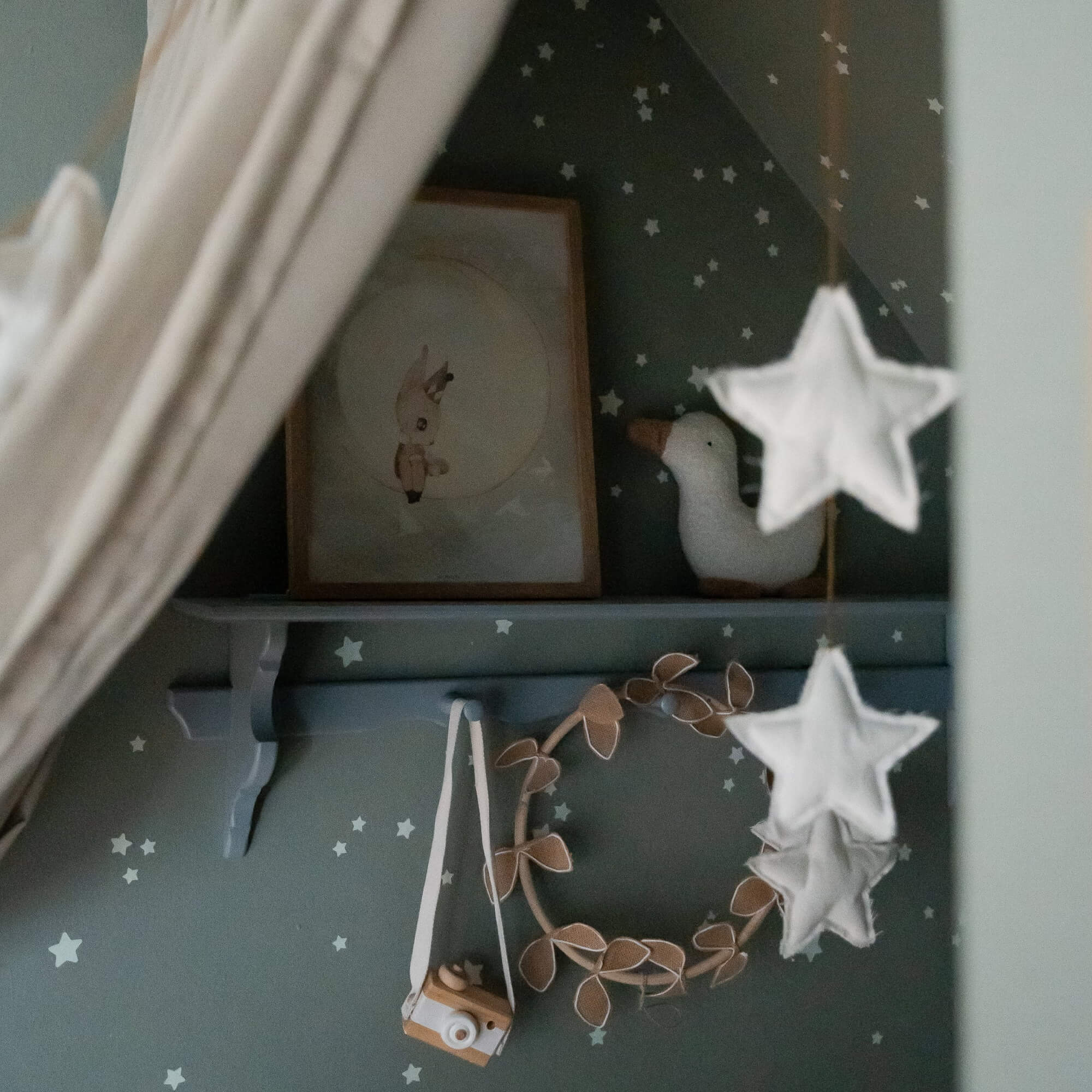 Décoration de chambre enfant avec étoiles blanches, canard en peluche et appareil photo en bois sur fond vert