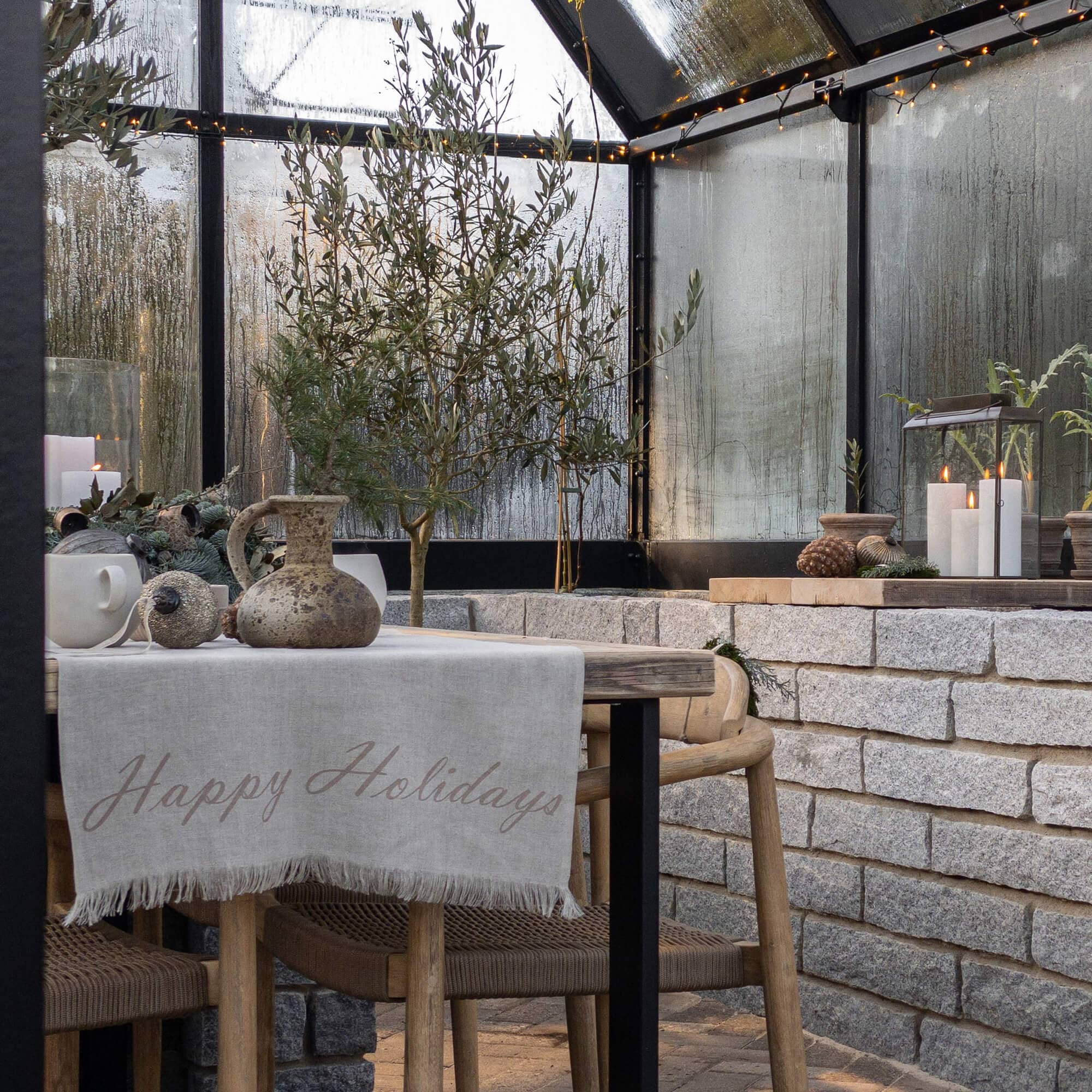 Coin chaleureux avec table en bois, nappe en lin et décorations de Noël dans une serre vitrée