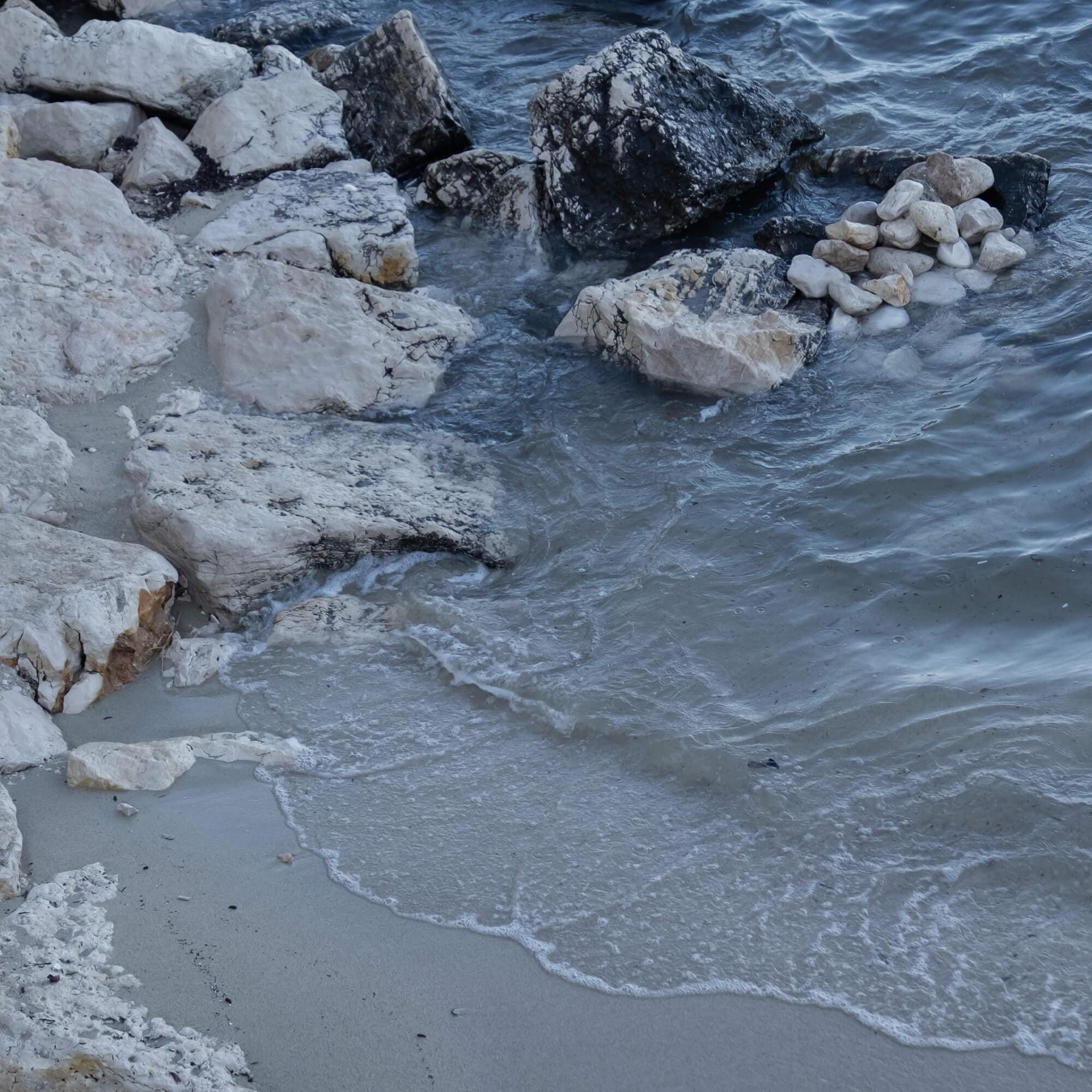 Rivage avec rochers clairs et foncés et vagues s'écrasant sur le sable humide