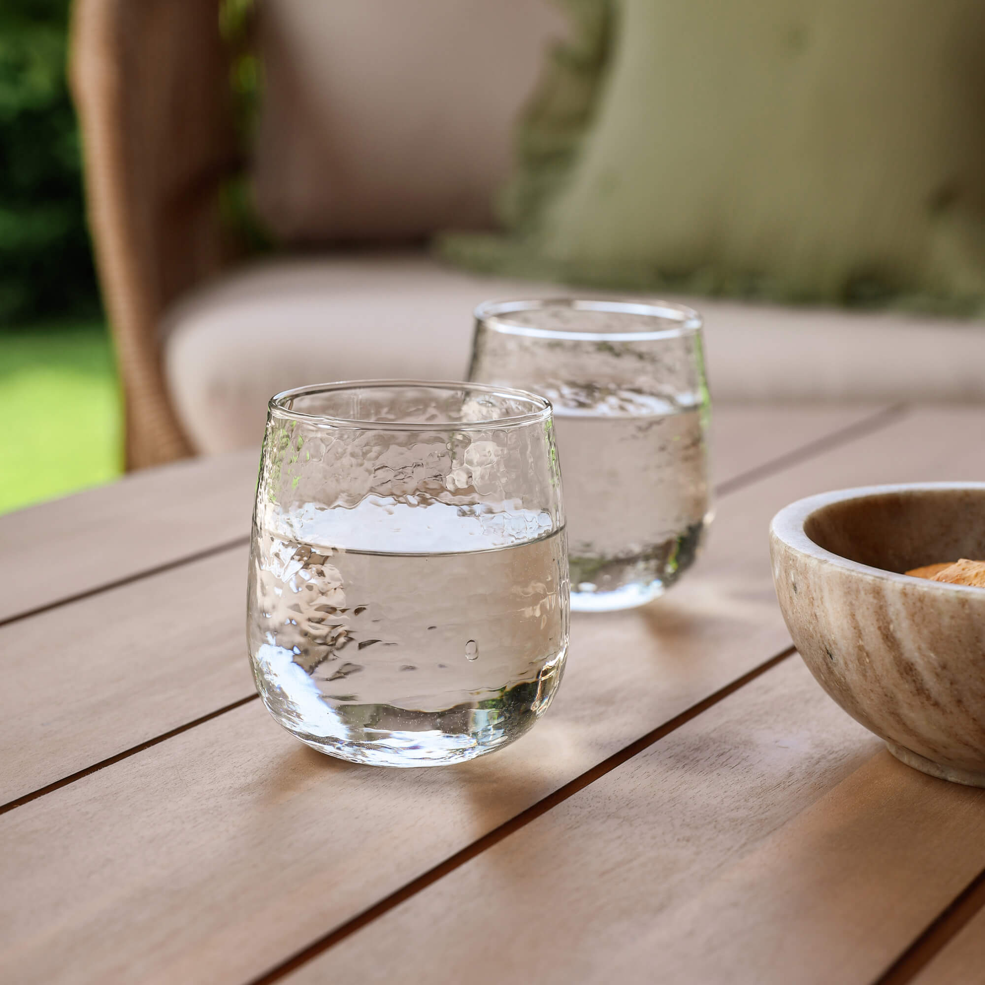 Deux verres transparents d'eau sur une table en bois dans un jardin avec un bol en pierre