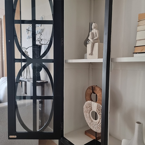 Vitrine en métal noir avec étagères décoratives et sculptures dans un salon lumineux