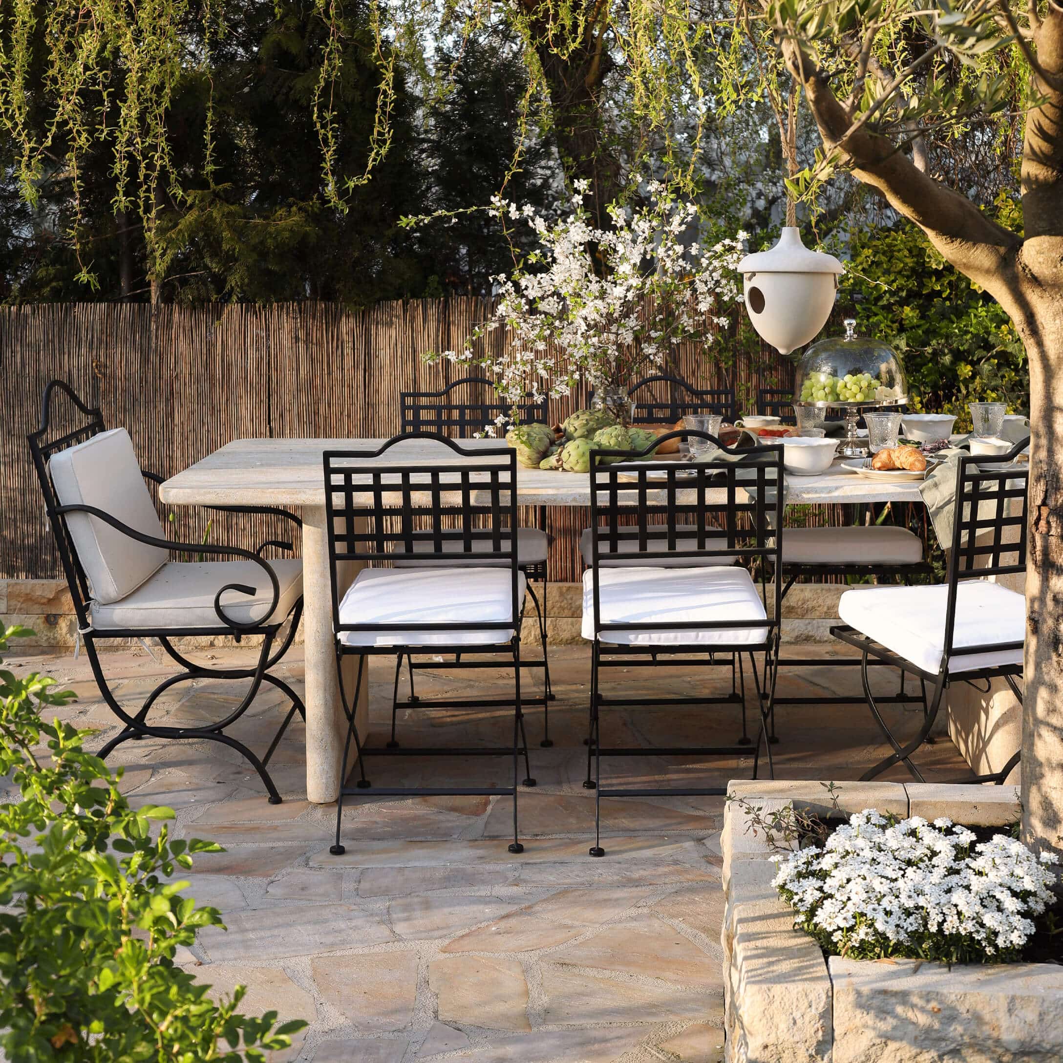 Ensemble de mobilier de jardin avec chaises en métal noir et table en pierre claire sur terrasse ensoleillée