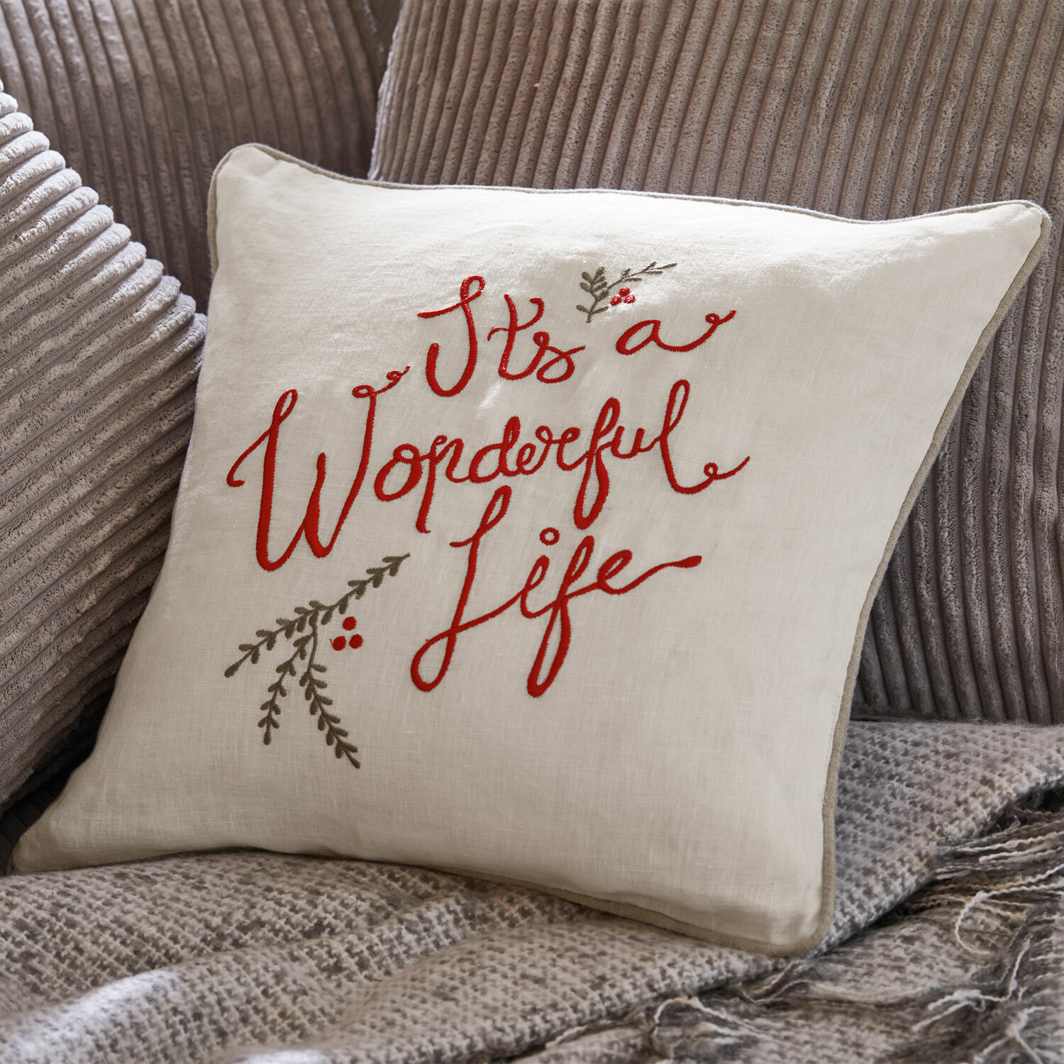 Housse de coussin Wonderful Coussin beige en lin avec broderie rouge "It's a Wonderful Life" sur tissu gris côtelé.