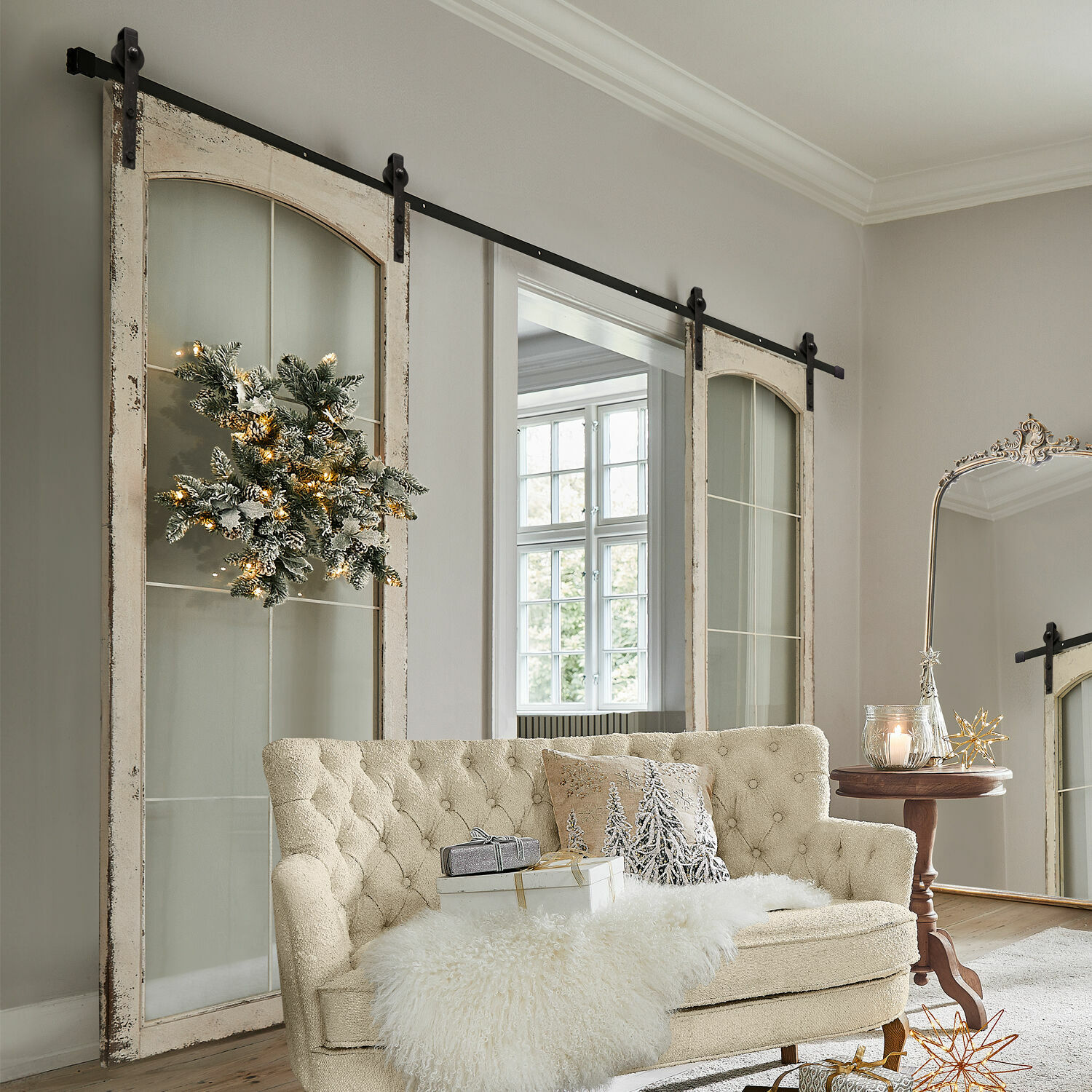 Double porte coulissante Incles Canapé beige capitonné avec plaid en fausse fourrure et décorations de Noël dans un salon lumineux avec portes coulissantes