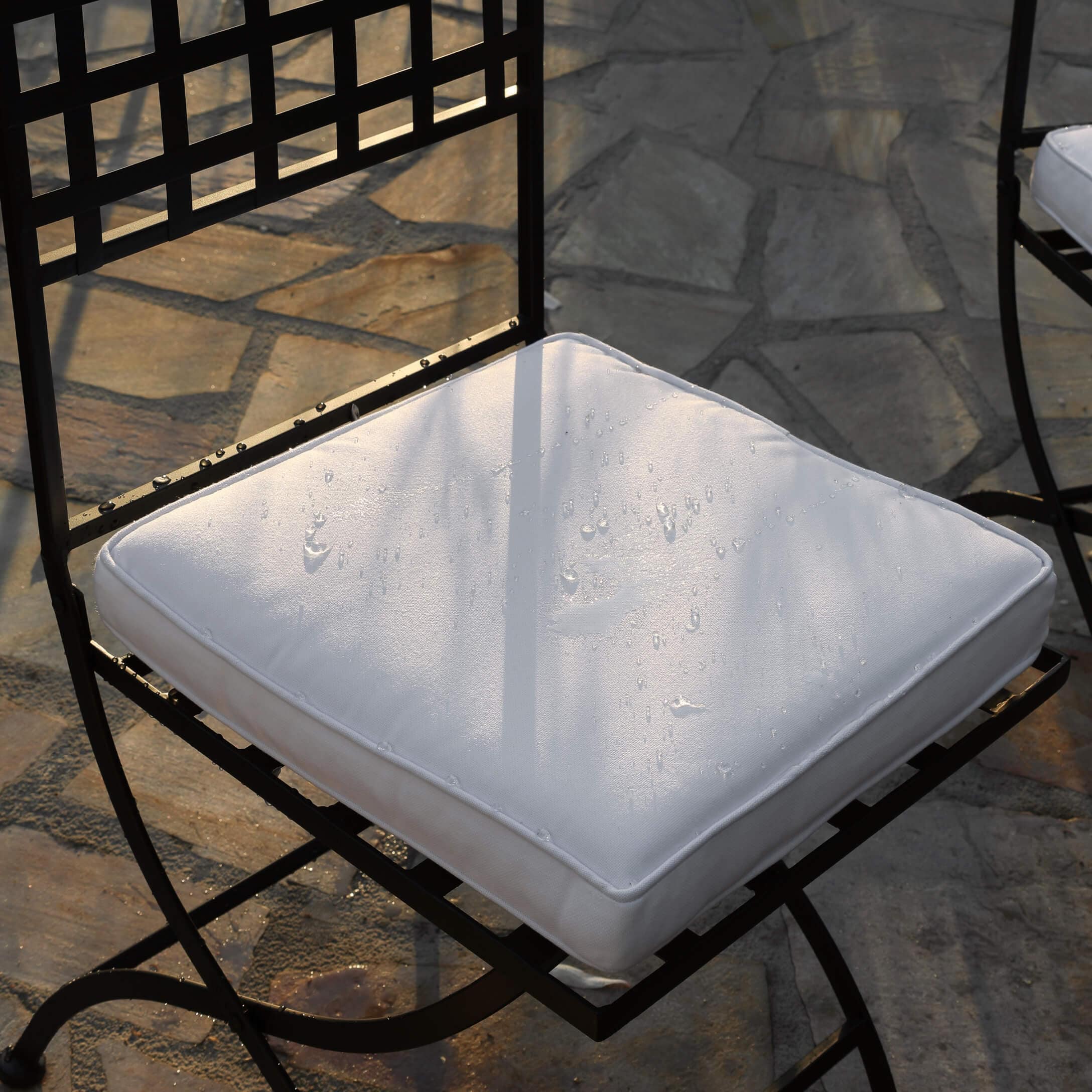 Coussin blanc imperméable sur chaise en métal noir posée sur sol en pierre