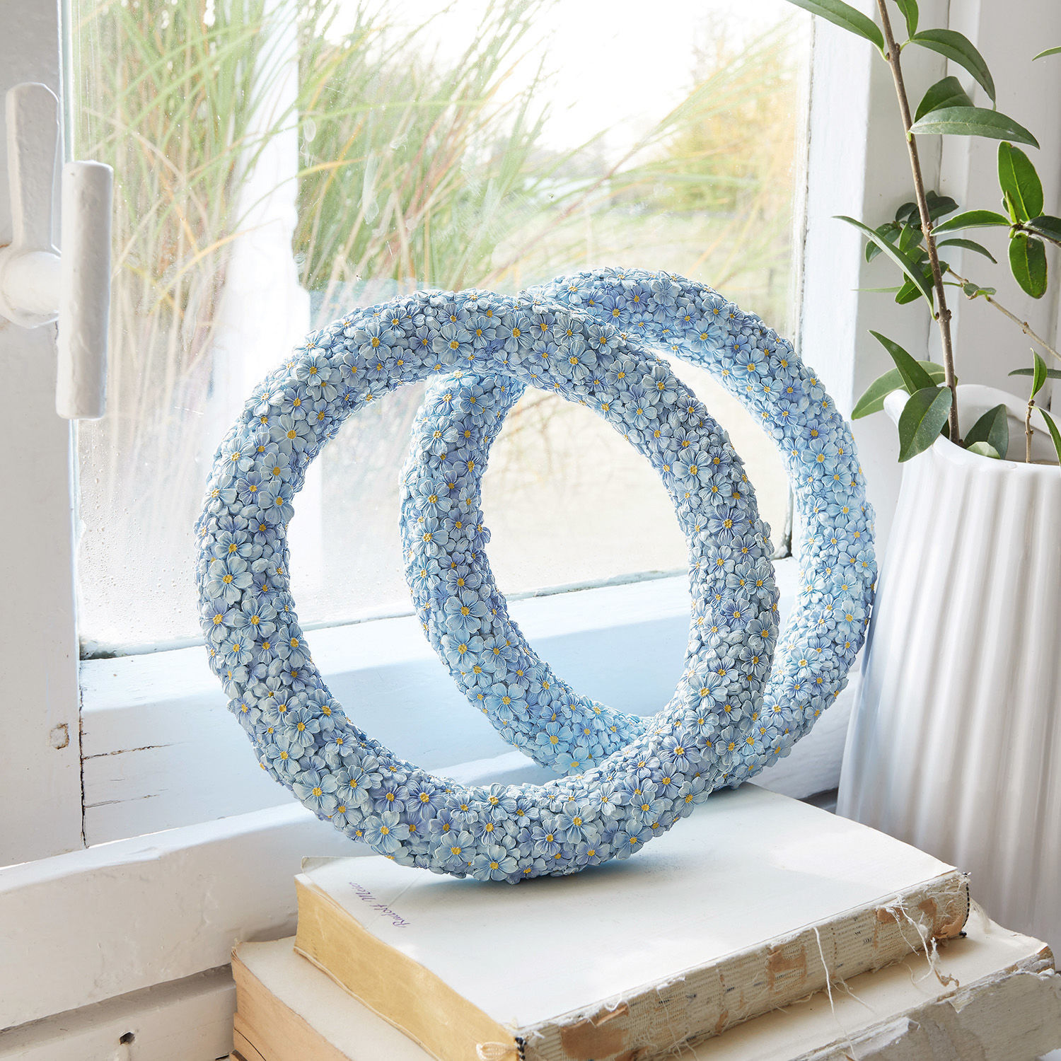 Lot de 2 couronnes Rigaud Sculpture décorative bleue en résine avec fleurs posée sur des livres près d'une fenêtre, décoration intérieure