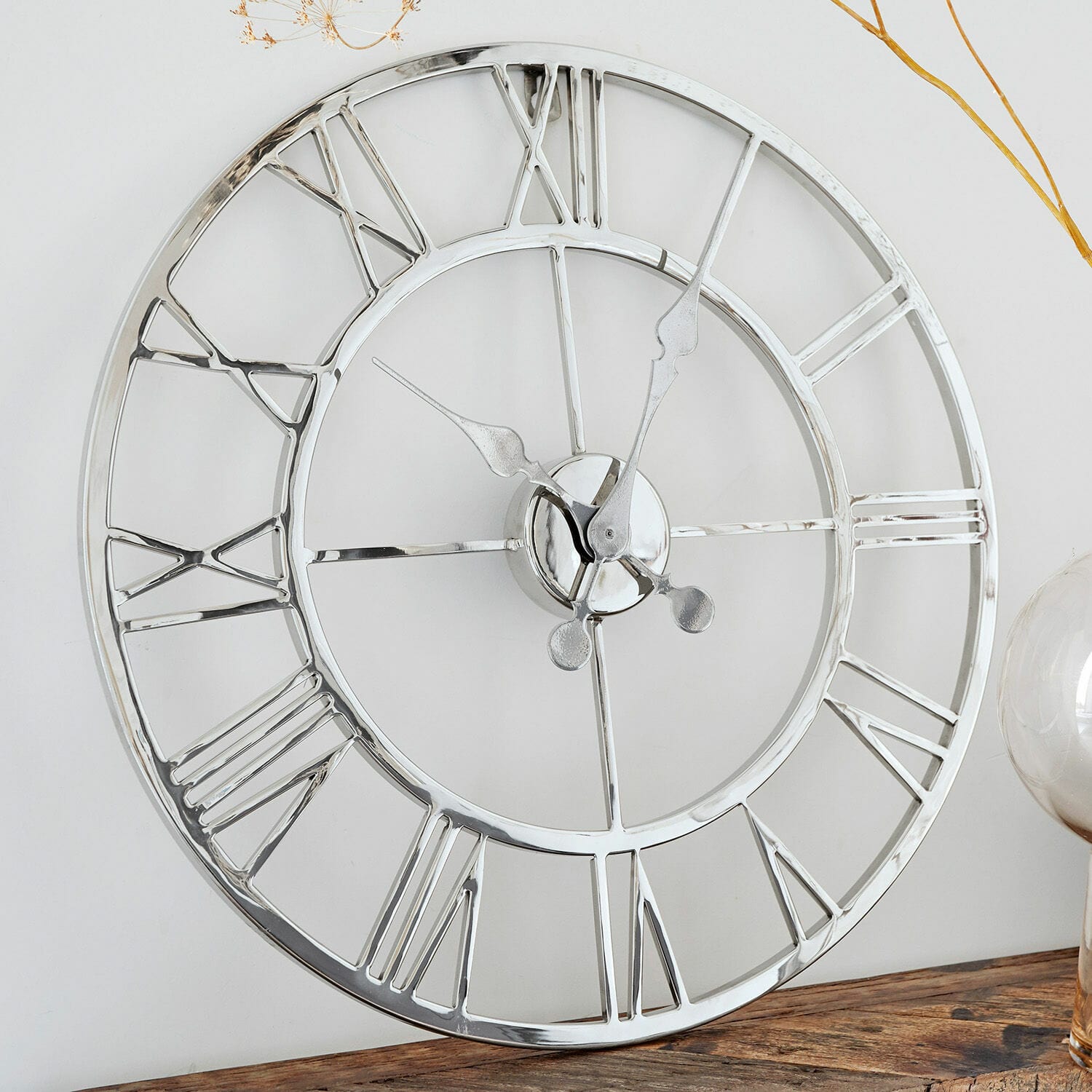 Horloge Houston Horloge murale ronde en métal argenté avec chiffres romains posée sur une table en bois