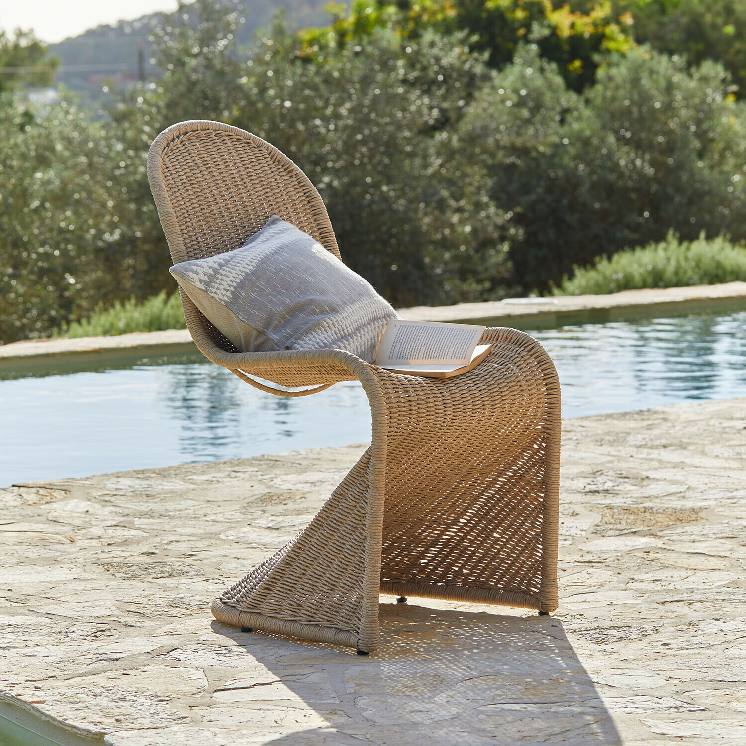 Chaise Melari Chaise d'extérieur en rotin couleur naturelle avec coussin et livre au bord de la piscine