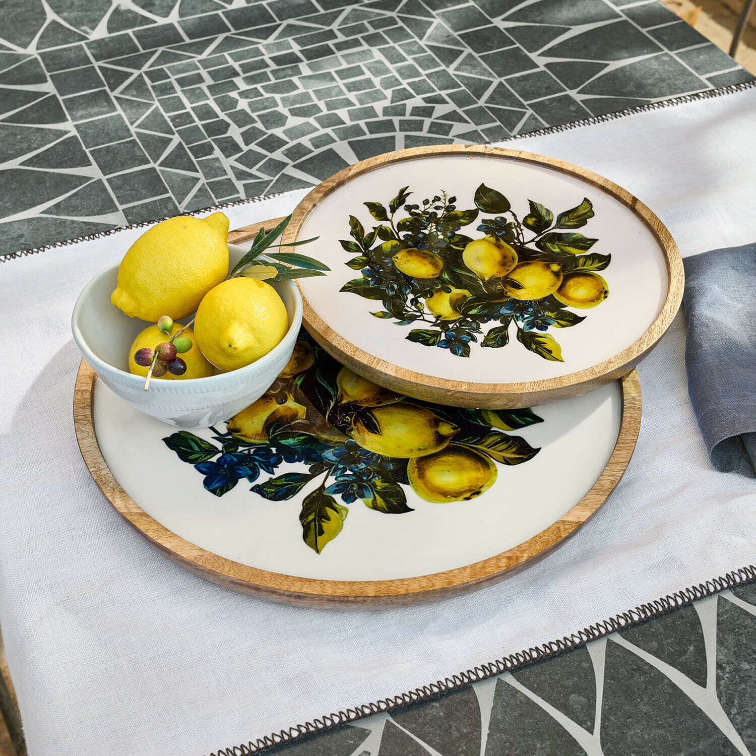 Lot de 2 plateaux Solianne Deux plateaux ronds en bois et céramique avec motif citron sur fond blanc sur une table en mosaïque